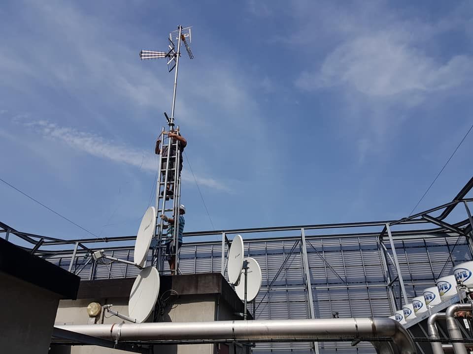 Tour de téléphonie mobile avec antennes et paraboles au-dessus d'un toit sous un ciel bleu.