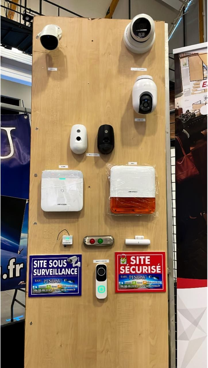 Panneau de démonstration de sécurité avec plusieurs caméras, capteurs et panneaux de surveillance de site français sur un panneau en bois.