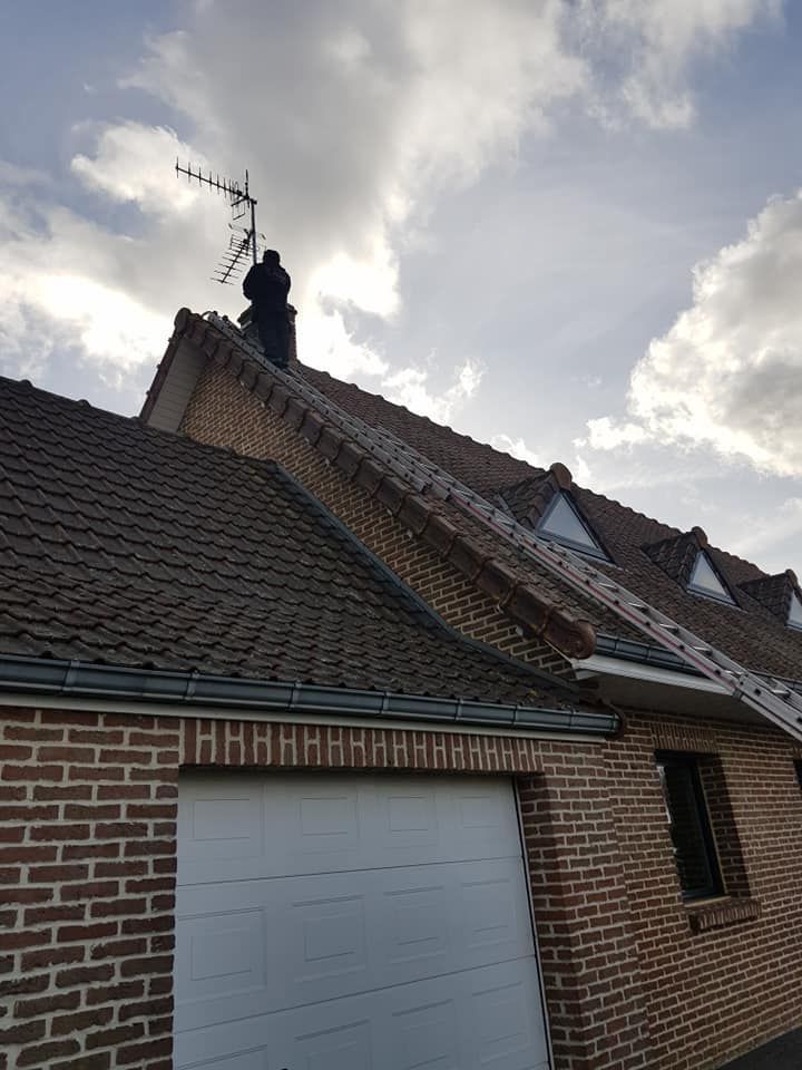 Maison en briques avec toit de tuiles, porte de garage et antenne de télévision.