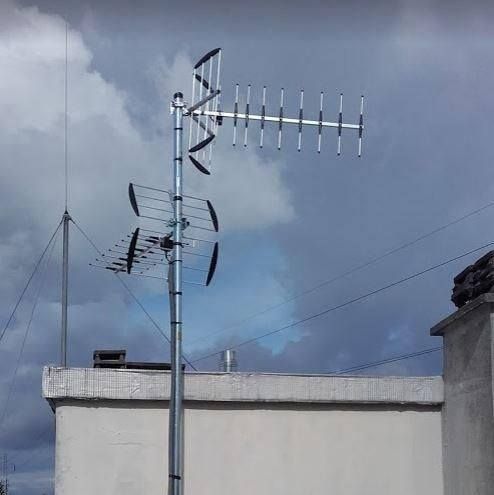 Antennes de télévision et paraboles sur le toit, se détachant sur un ciel nuageux au-dessus d'un mur blanc.