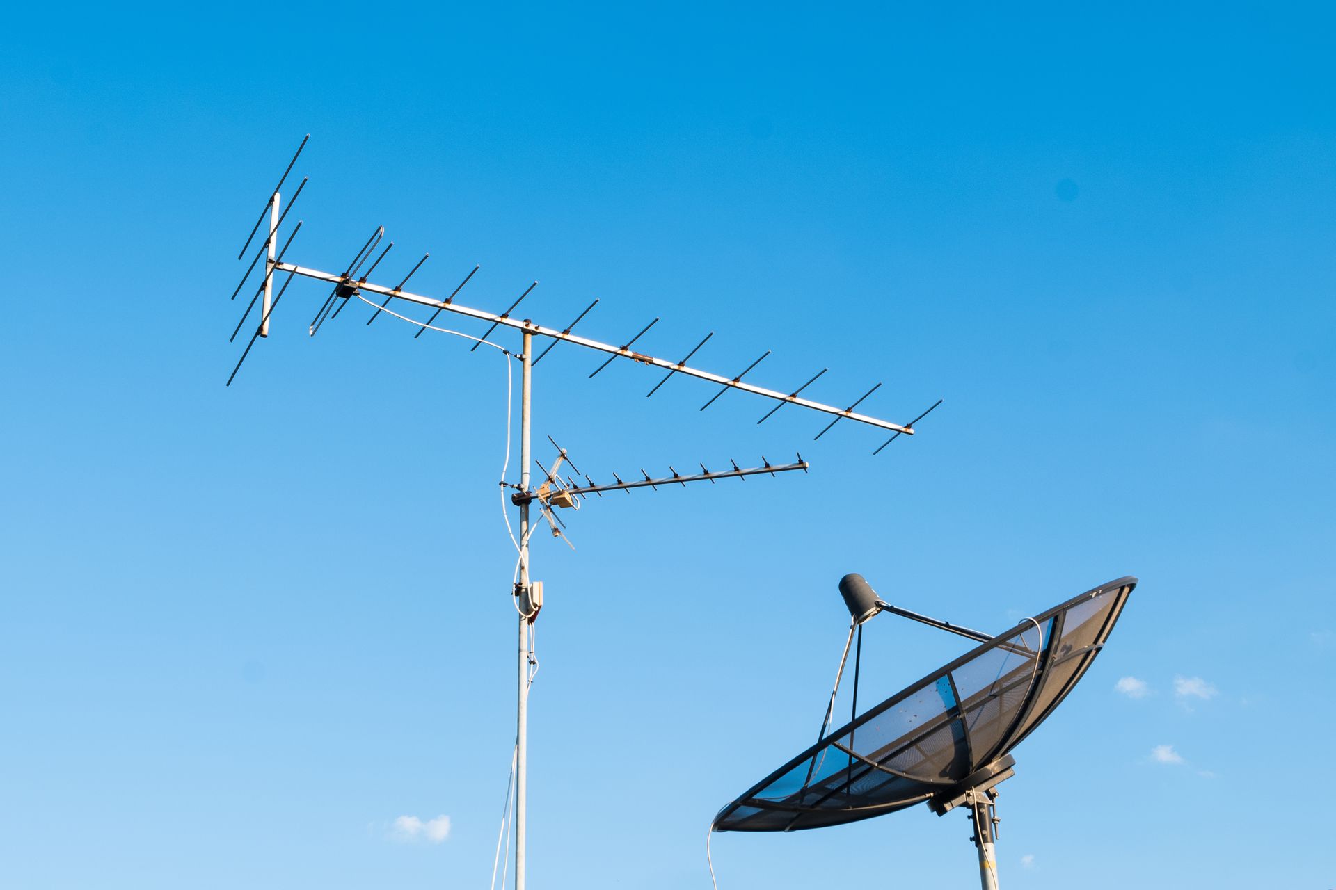 Deux antennes sur le toit se détachant sur un ciel bleu azur, dont une grande parabole.