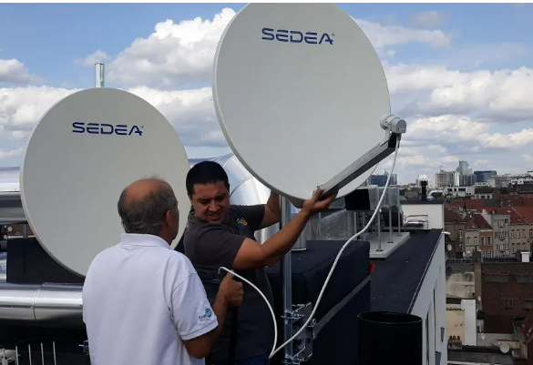 Deux hommes sur un toit ajustent des antennes paraboliques blanches Sedea sur fond de silhouette urbaine.