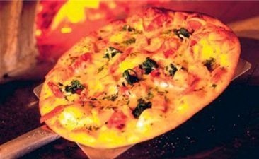 Pizza en pala de horno de leña, corteza dorada, queso, espinacas y aderezos.