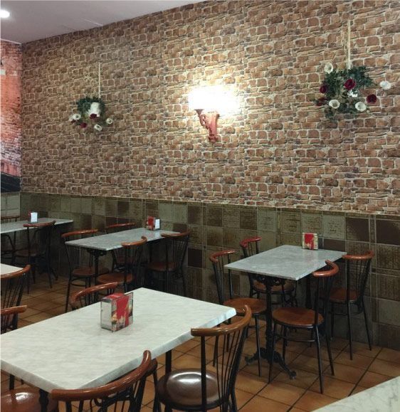Interior del restaurante: pared de ladrillo, mesas, sillas y decoración. Iluminación cálida y combinación de colores marrón y blanco.