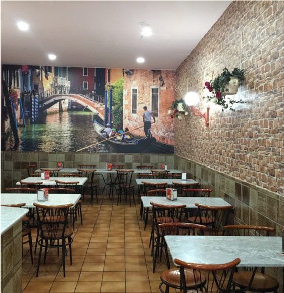 Interior de restaurante con mesas, sillas, pared de ladrillo y mural de Venecia.