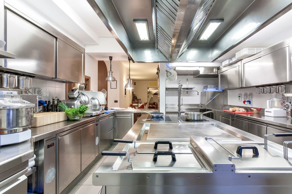 Une cuisine commerciale professionnelle en acier inoxydable avec comptoirs, appareils de cuisson et hotte aspirante.
