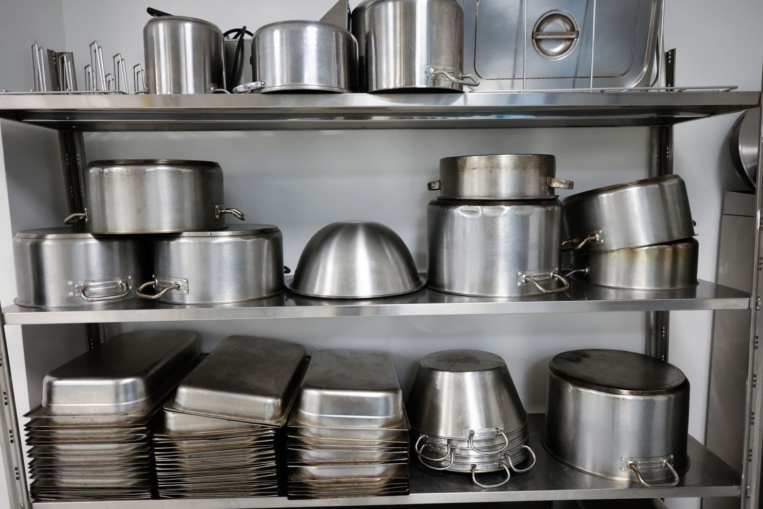 Une étagère en acier inoxydable remplie de piles bien rangées de casseroles, poêles et plaques de cuisson en métal.