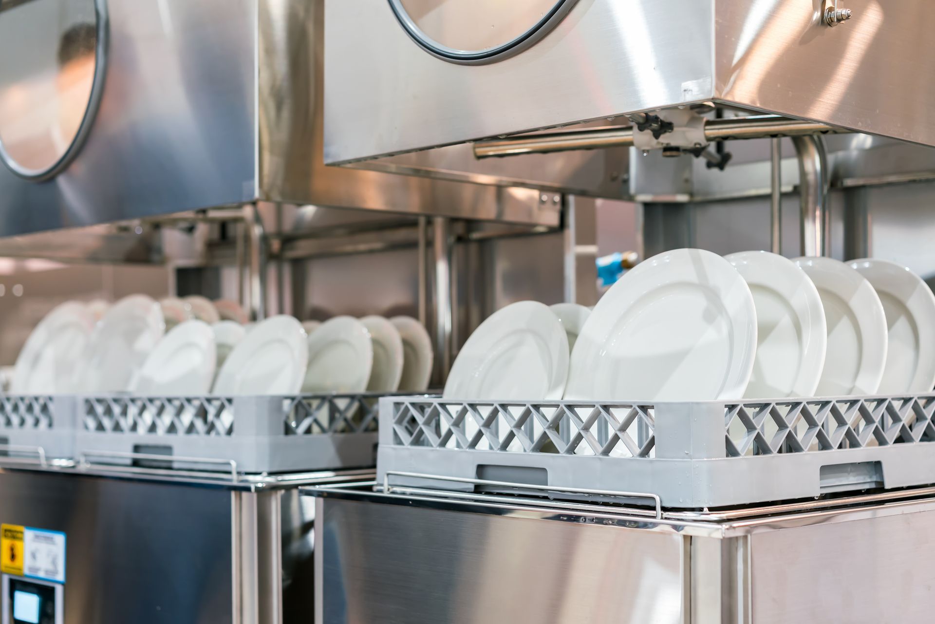 Deux étagères grises remplies d'assiettes blanches propres sont posées sur des lave-vaisselle industriels en acier inoxydable.