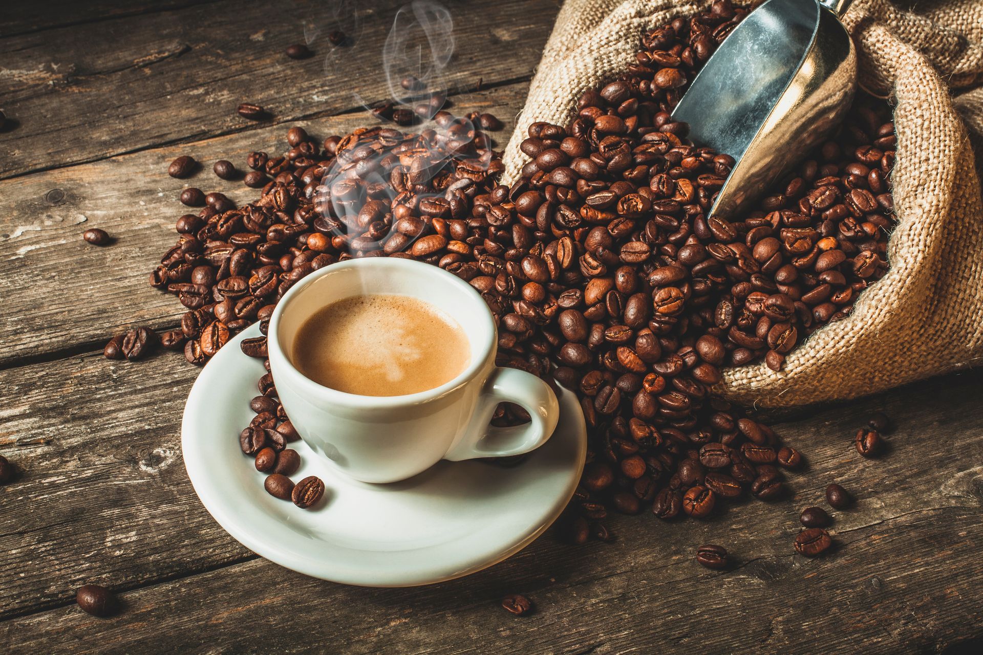 Une tasse de café fumante à côté d'un sac de jute débordant de grains de café torréfiés, sur une table rustique en bois.