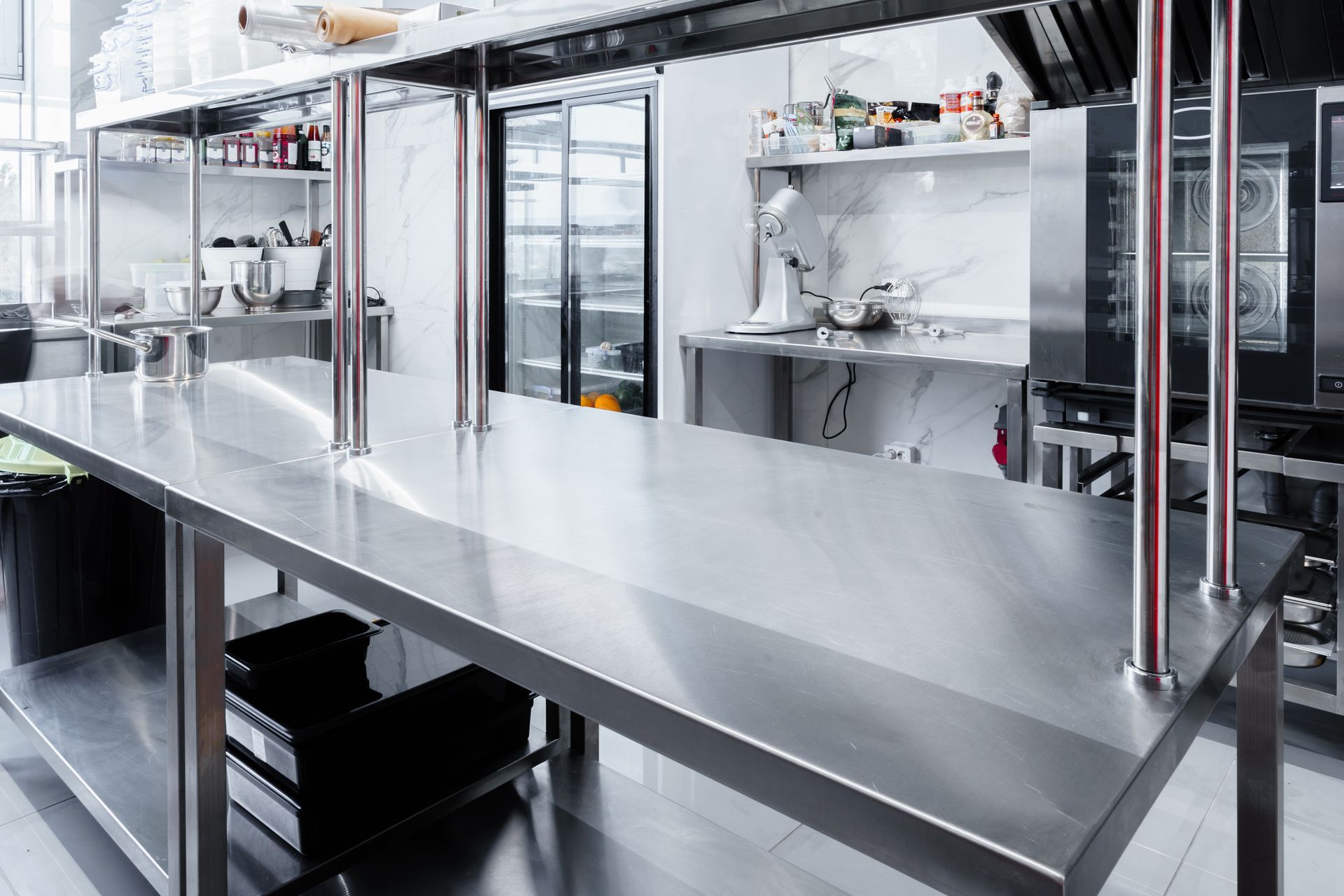 Un espace de travail de cuisine commerciale propre et en acier inoxydable, avec un comptoir de préparation, des étagères et des appareils professionnels.