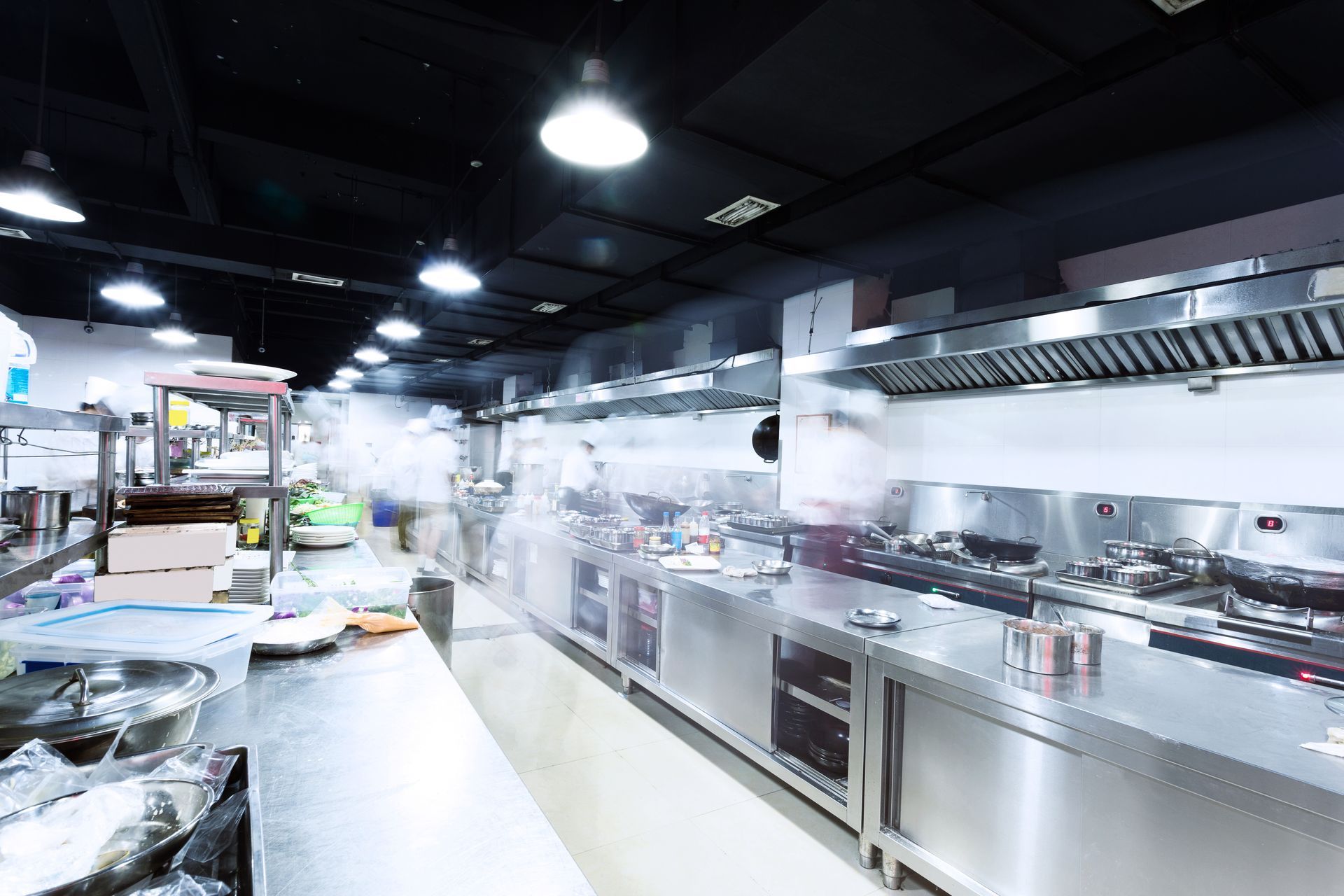 Vue floue de chefs travaillant dans une cuisine commerciale animée, aux murs en acier inoxydable.