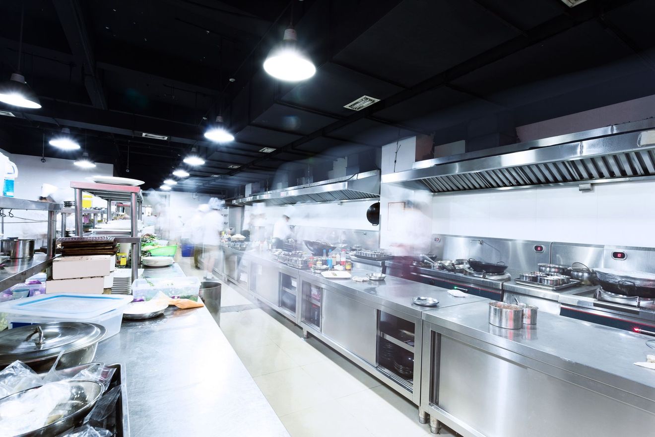 Vue floue de chefs travaillant dans une cuisine commerciale animée, aux murs en acier inoxydable.