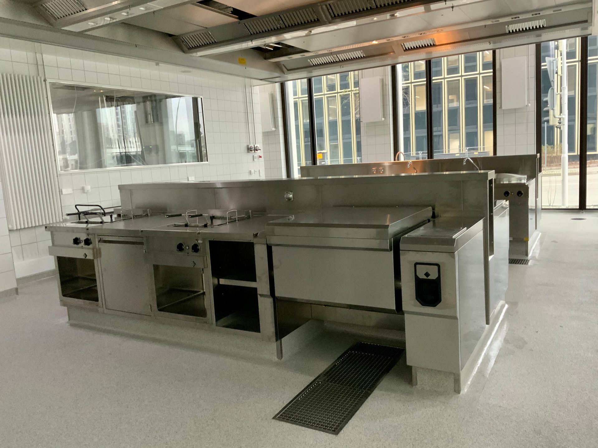 Eine große leere Küche mit Geräten aus Edelstahl und vielen Fenstern.