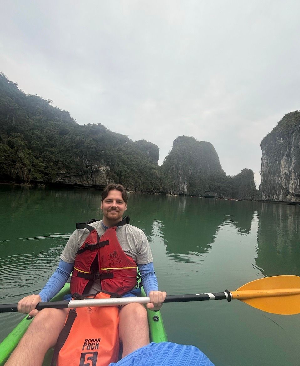 Man kayaking in green water, wearing a life vest, with limestone cliffs in the background.