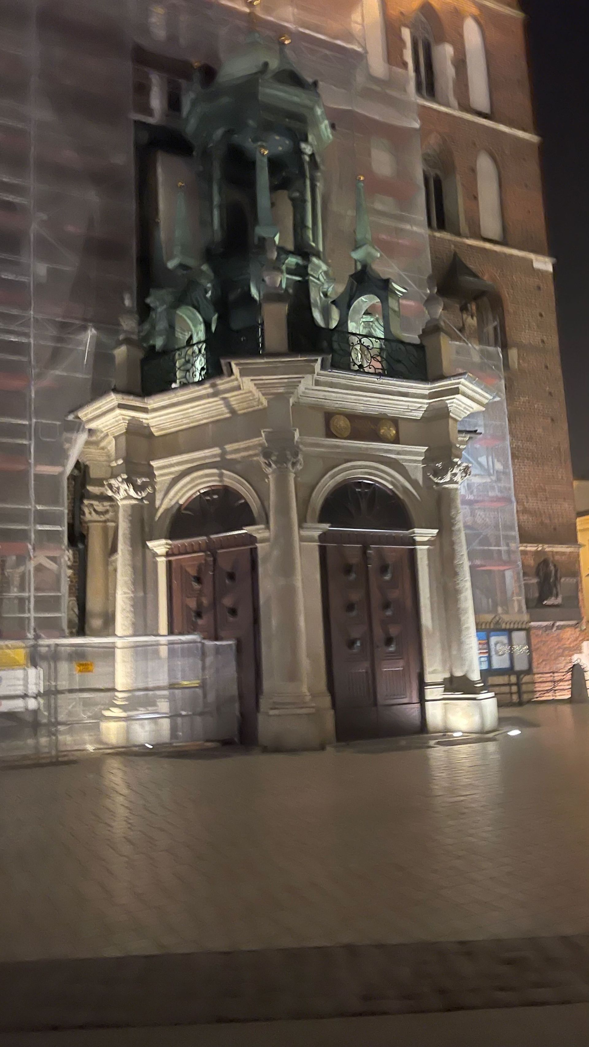 Facade of a building with two arched doorways, topped by a structure with sculptures, at night.