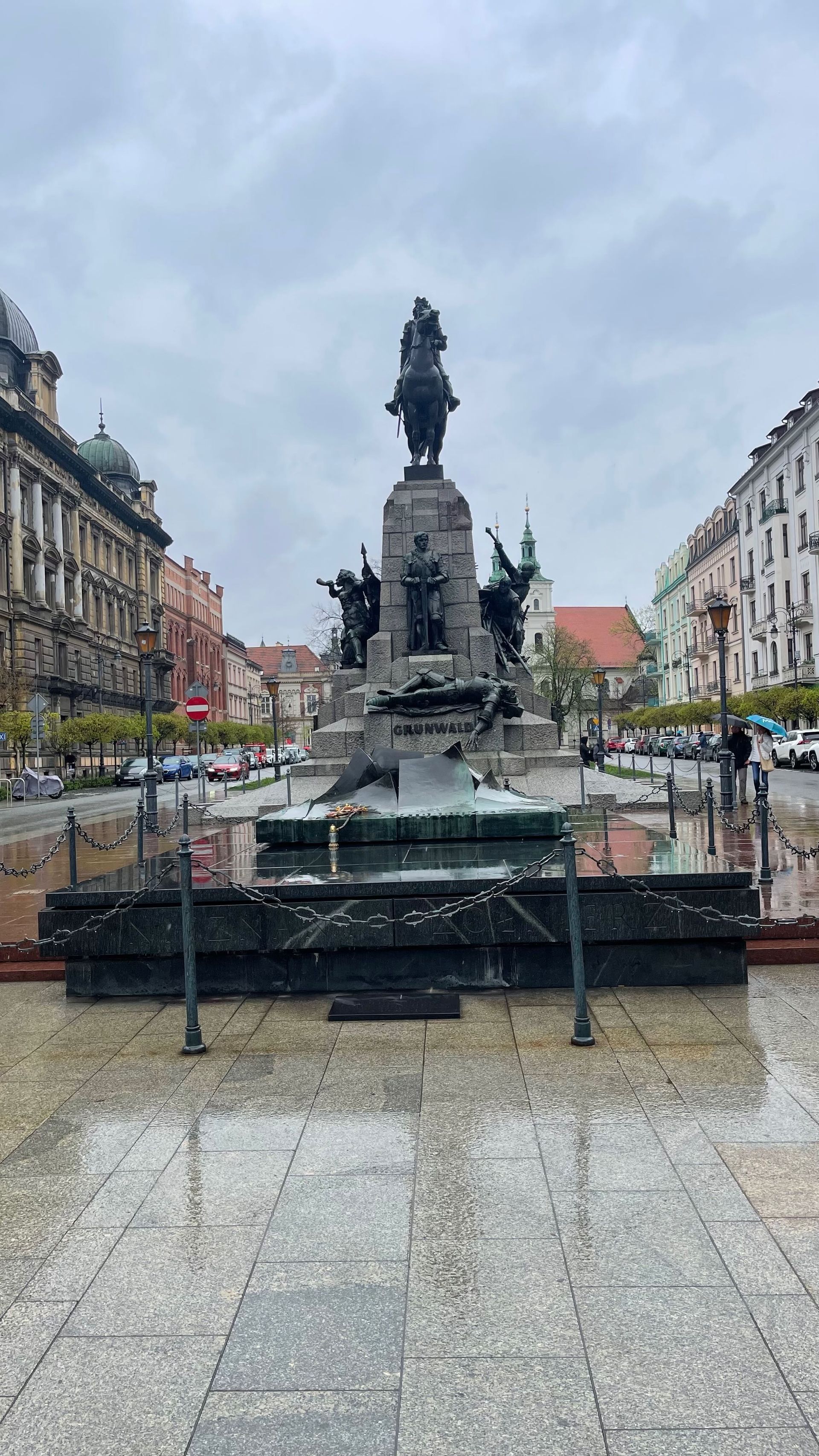 A statue of a man on horseback in a square in a city, rainy day.