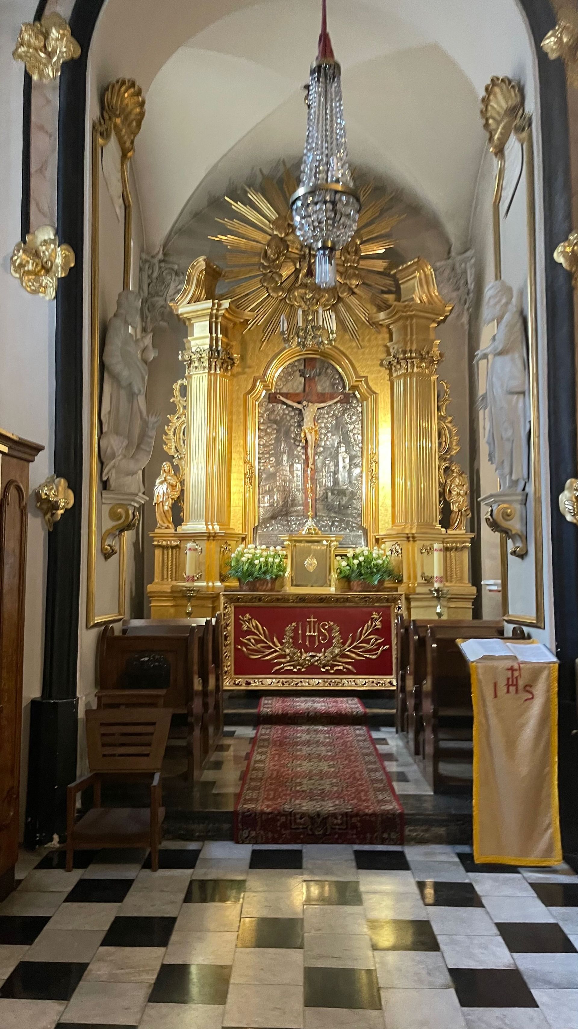 Golden altar in a church, with a crucifix. Red carpet leads to it. Checkerboard floor.