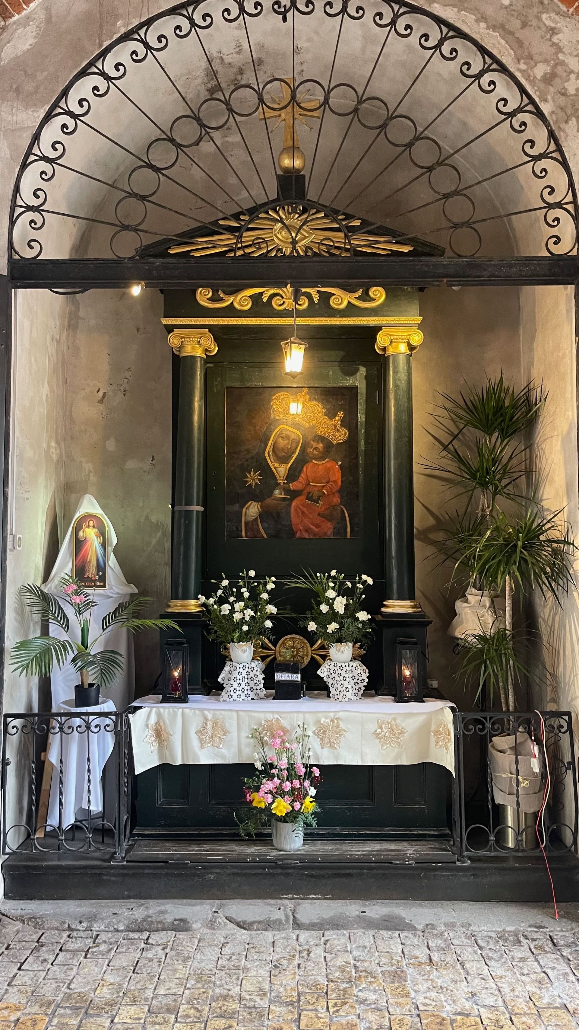 Altar inside a stone structure. Features a painting, flowers, candles, and decorative ironwork.