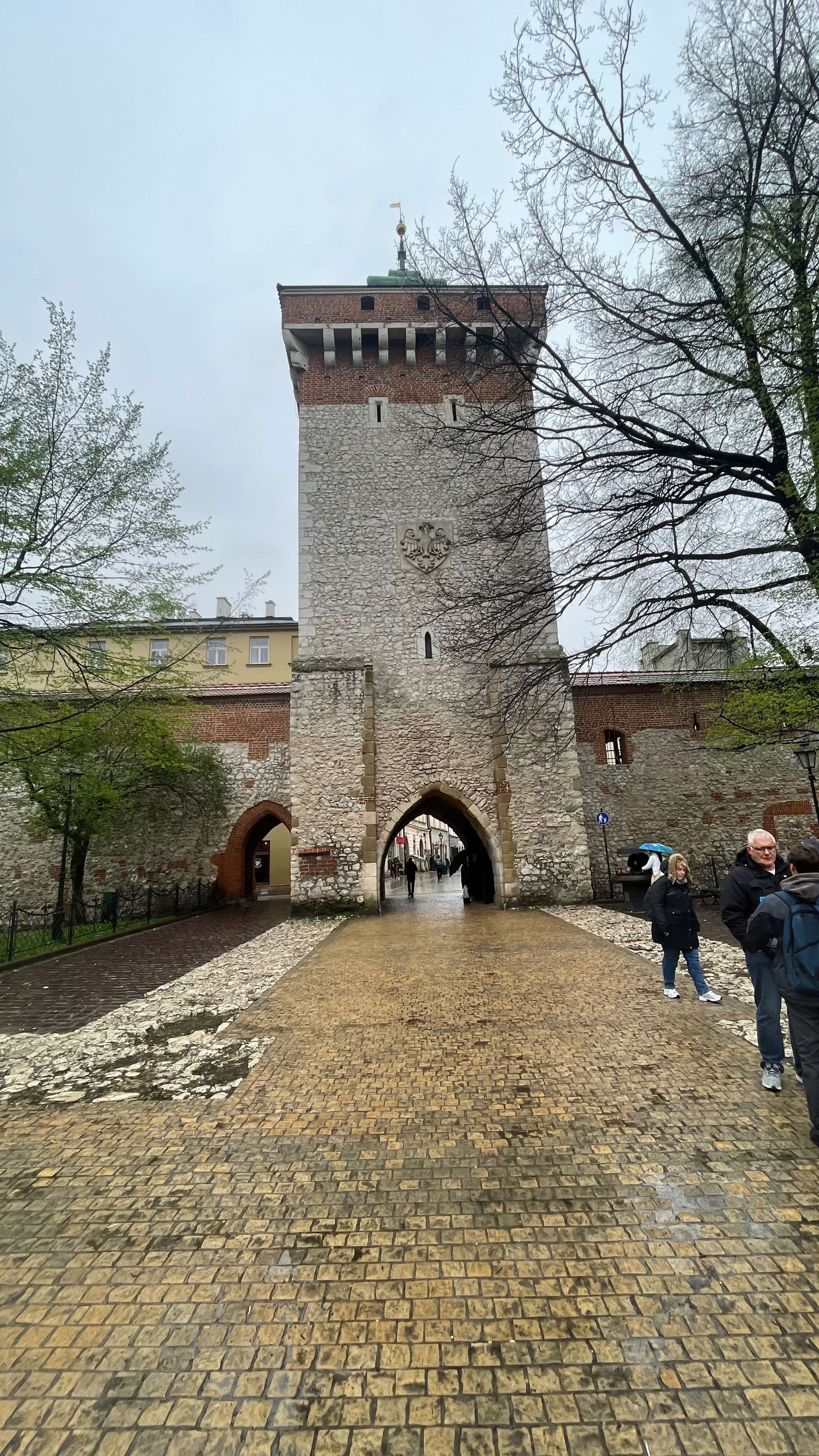 Medieval stone gate tower with archway entrance; people walking through it, overcast day.