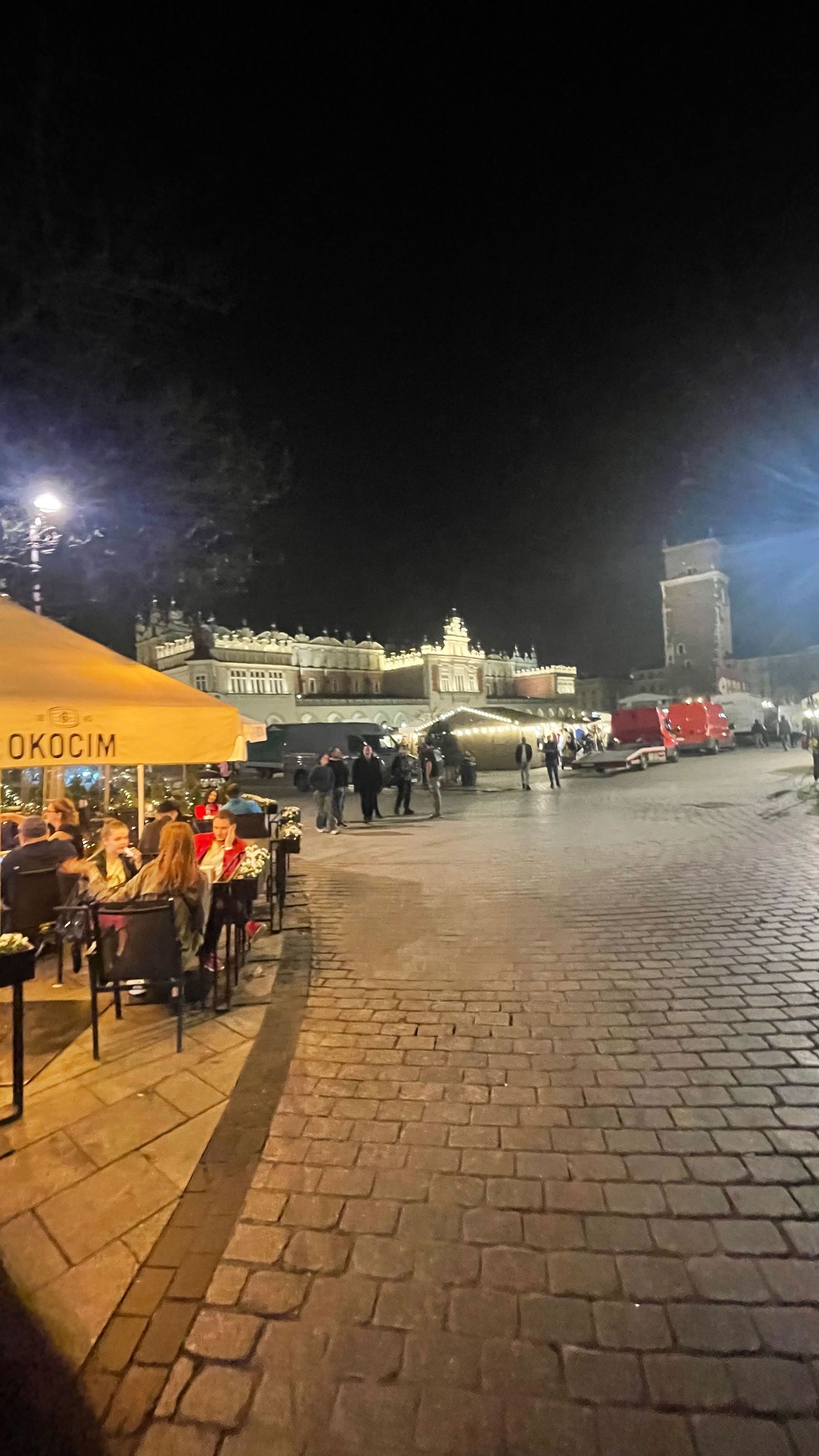 Cobblestone street at night with lit buildings, restaurant, and people.