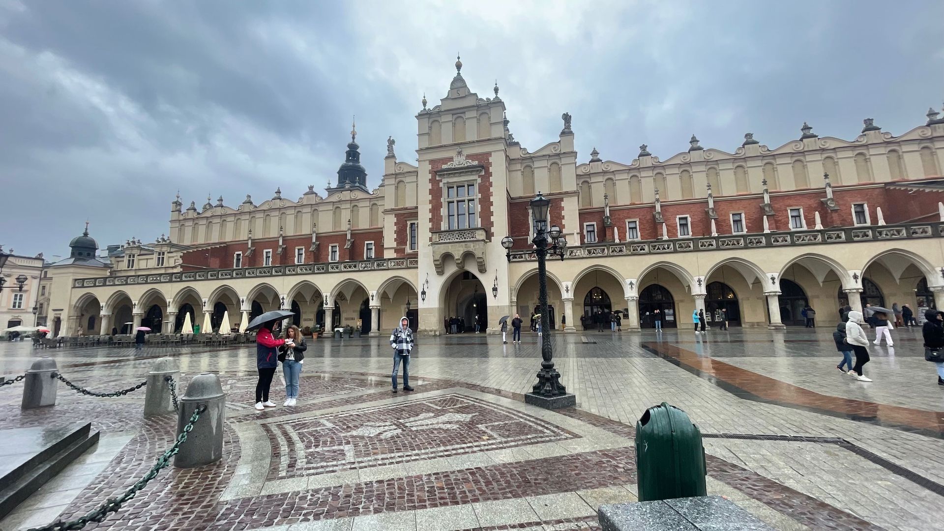 Kraków's Cloth Hall on a rainy day. People walk in the square, arched colonnade, cloudy sky.