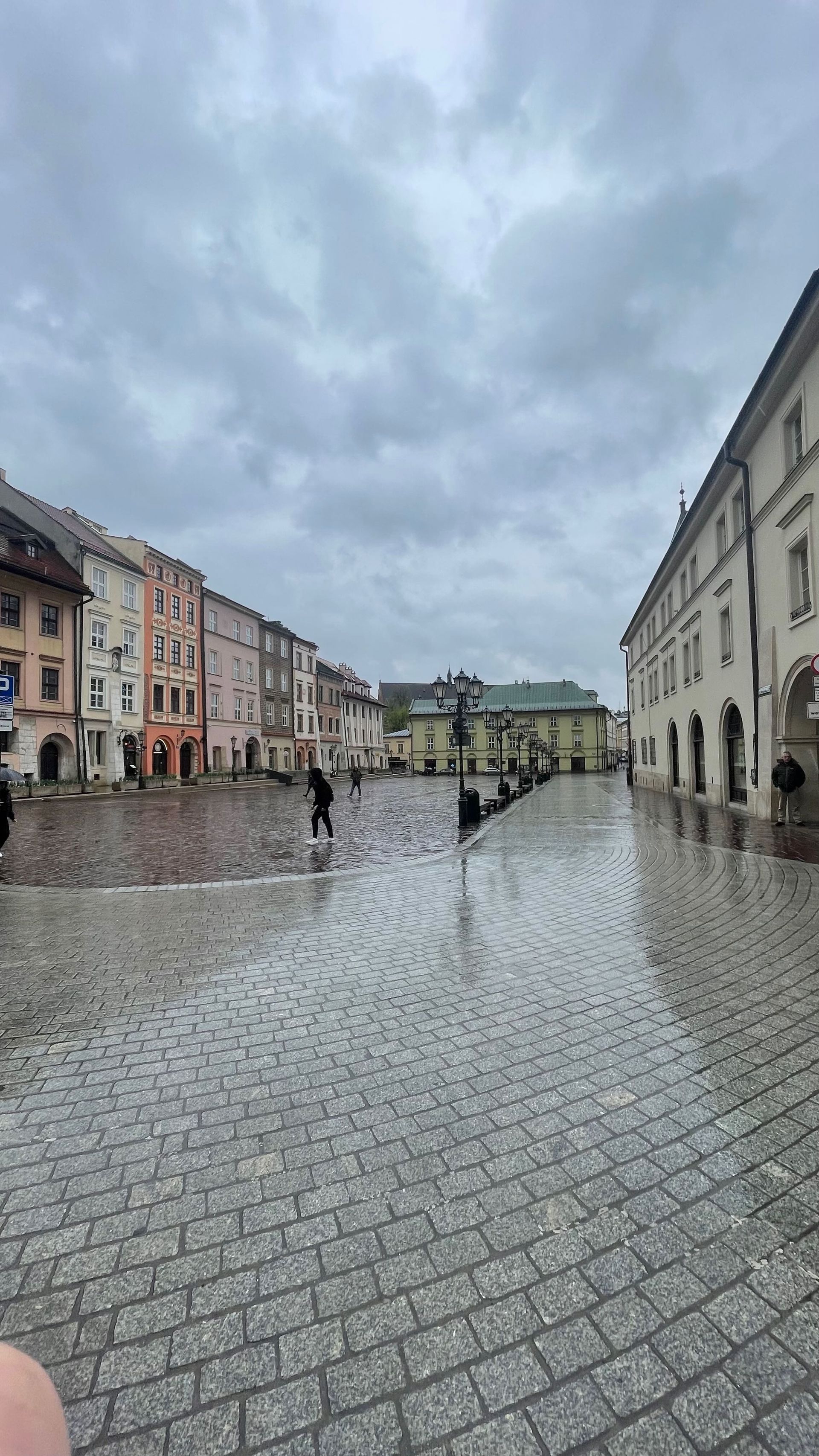 Cobblestone square with colorful buildings under a cloudy sky; a few people walk.