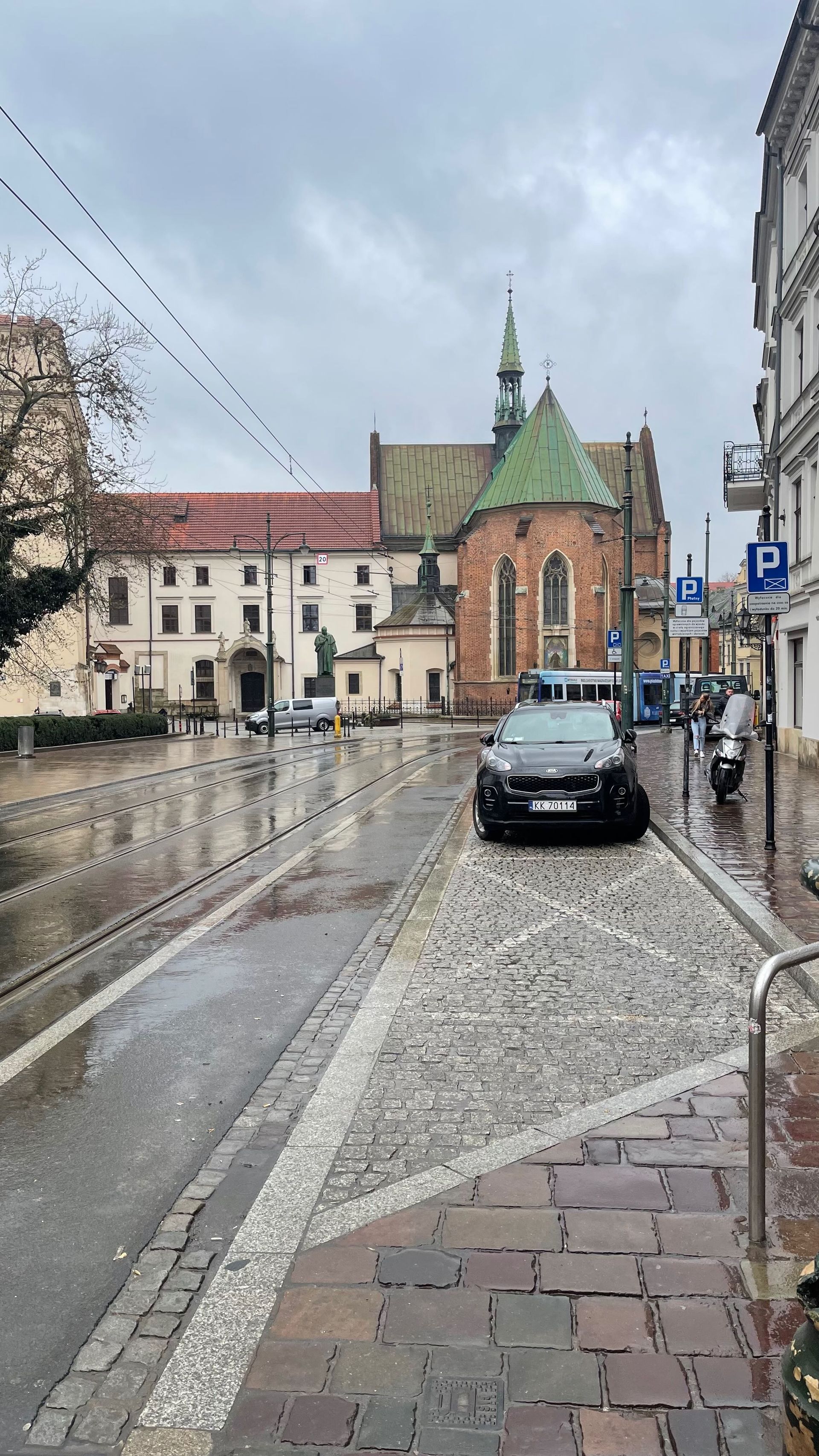 Cobblestone street with church and buildings on a rainy day in Kraków, Poland.