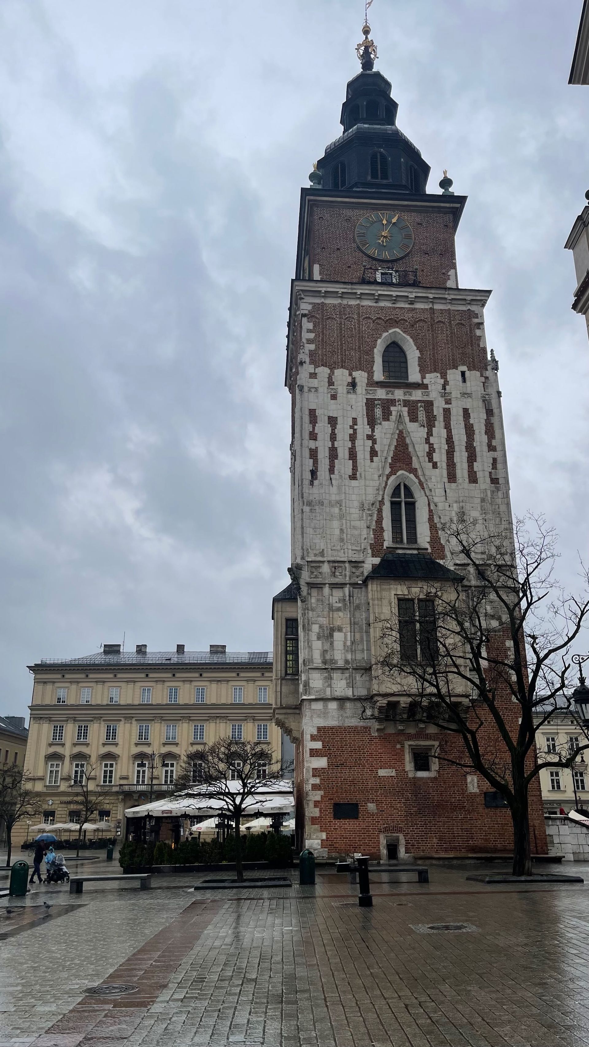Brick tower with clock, on a square in Krakow, Poland. Gray sky overhead.