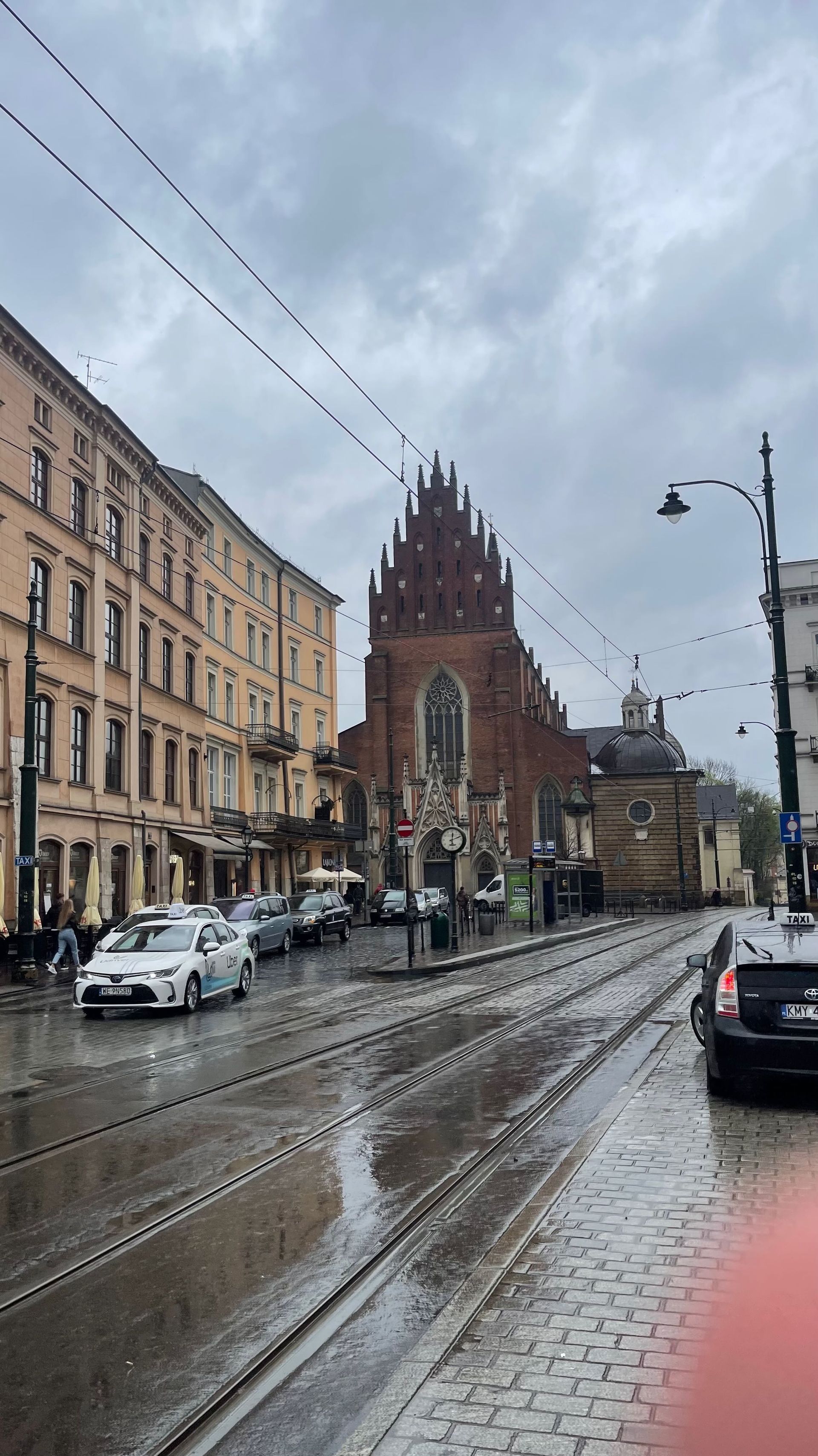 Street scene with church, wet cobblestone, cars, and overcast sky.