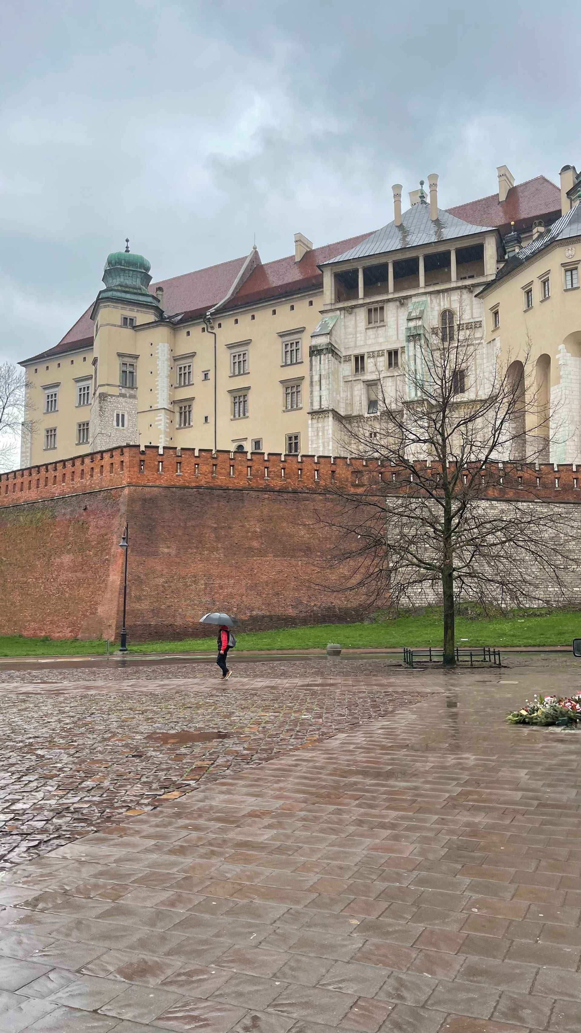 Wawel Castle in Kraków on a rainy day. A person with an umbrella walks on wet cobblestones.