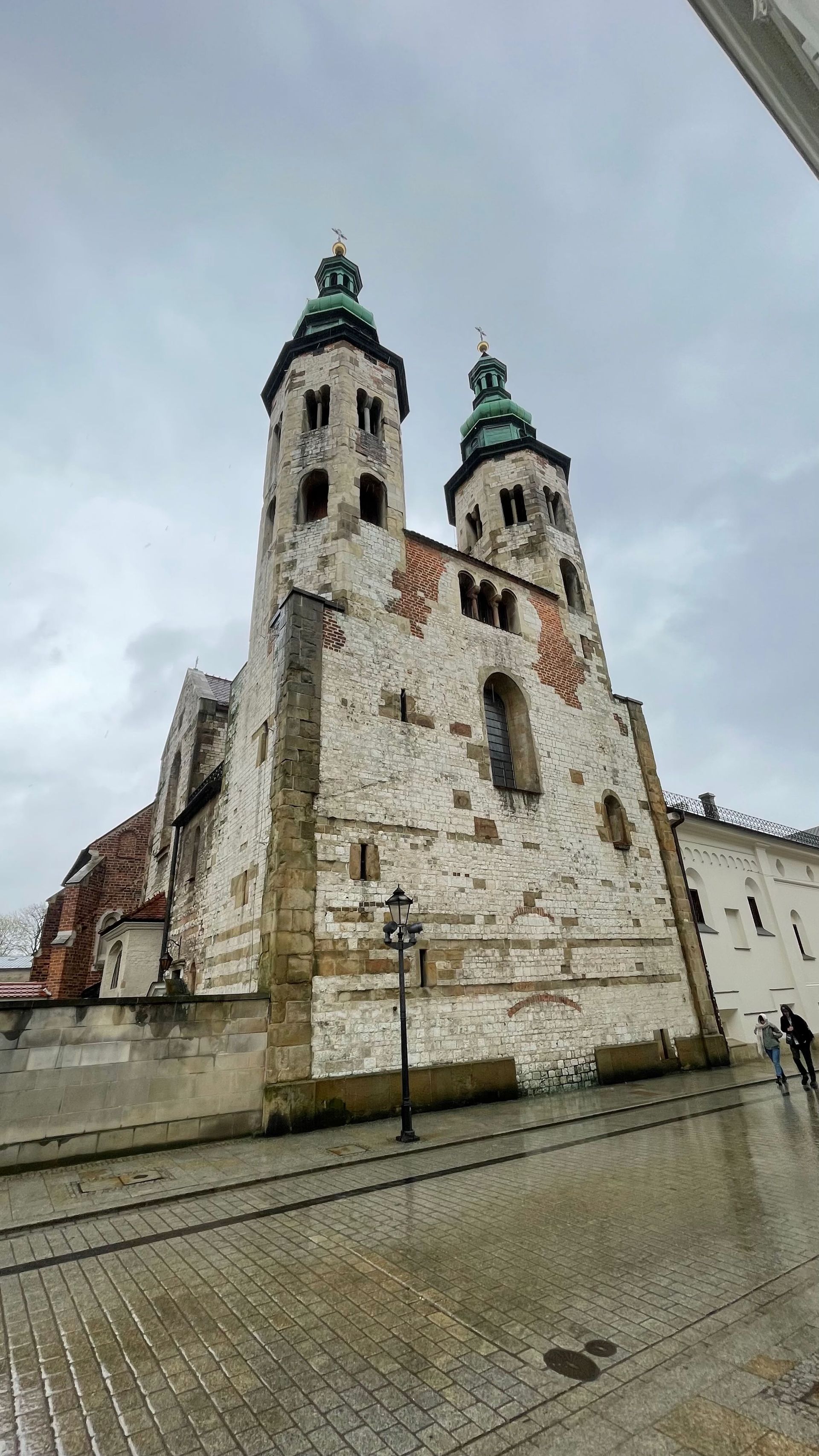 Two-towered, weathered stone church under a cloudy sky. Street lamp in front.