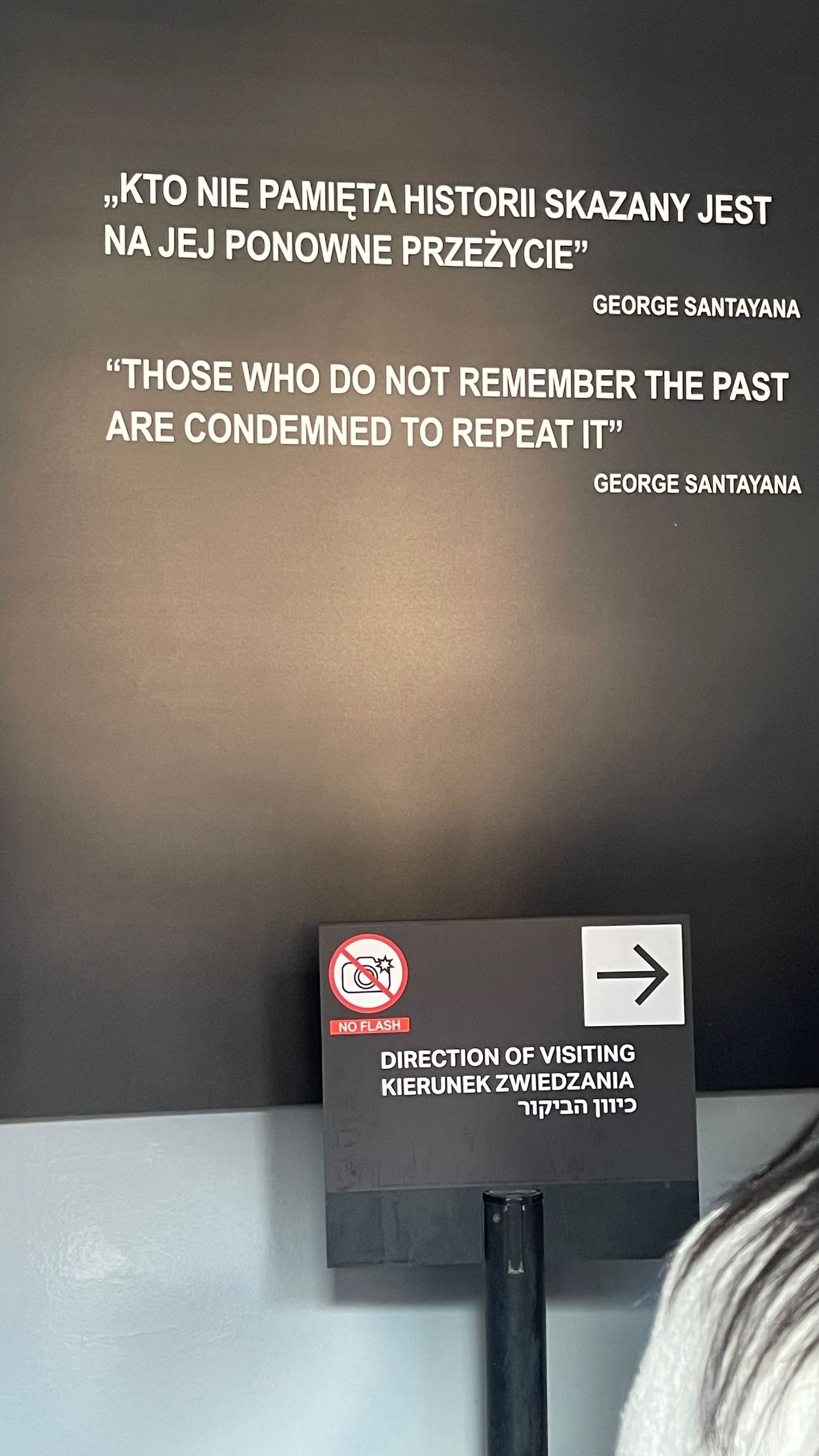 Black wall with quote in Polish and English, sign with arrow pointing right.