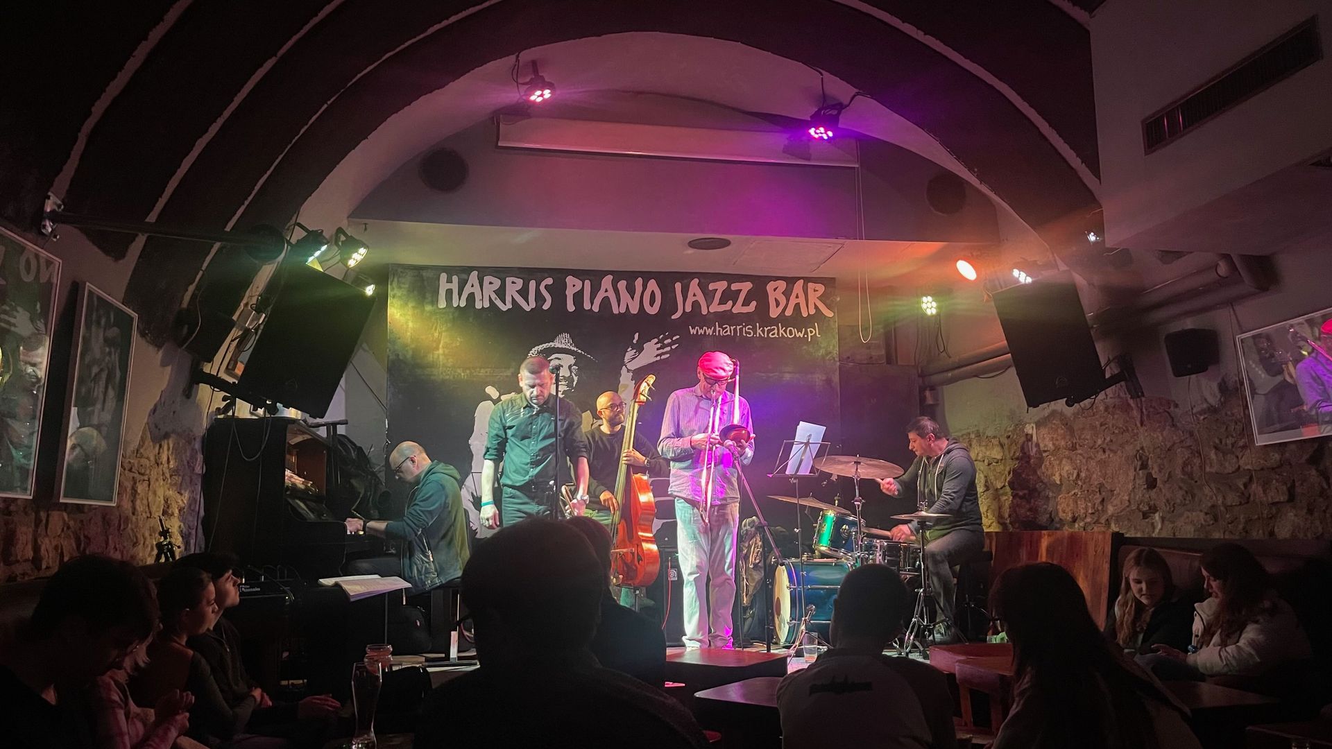 Jazz band performing on stage at Harris Piano Jazz Bar. Dim lighting, audience visible.