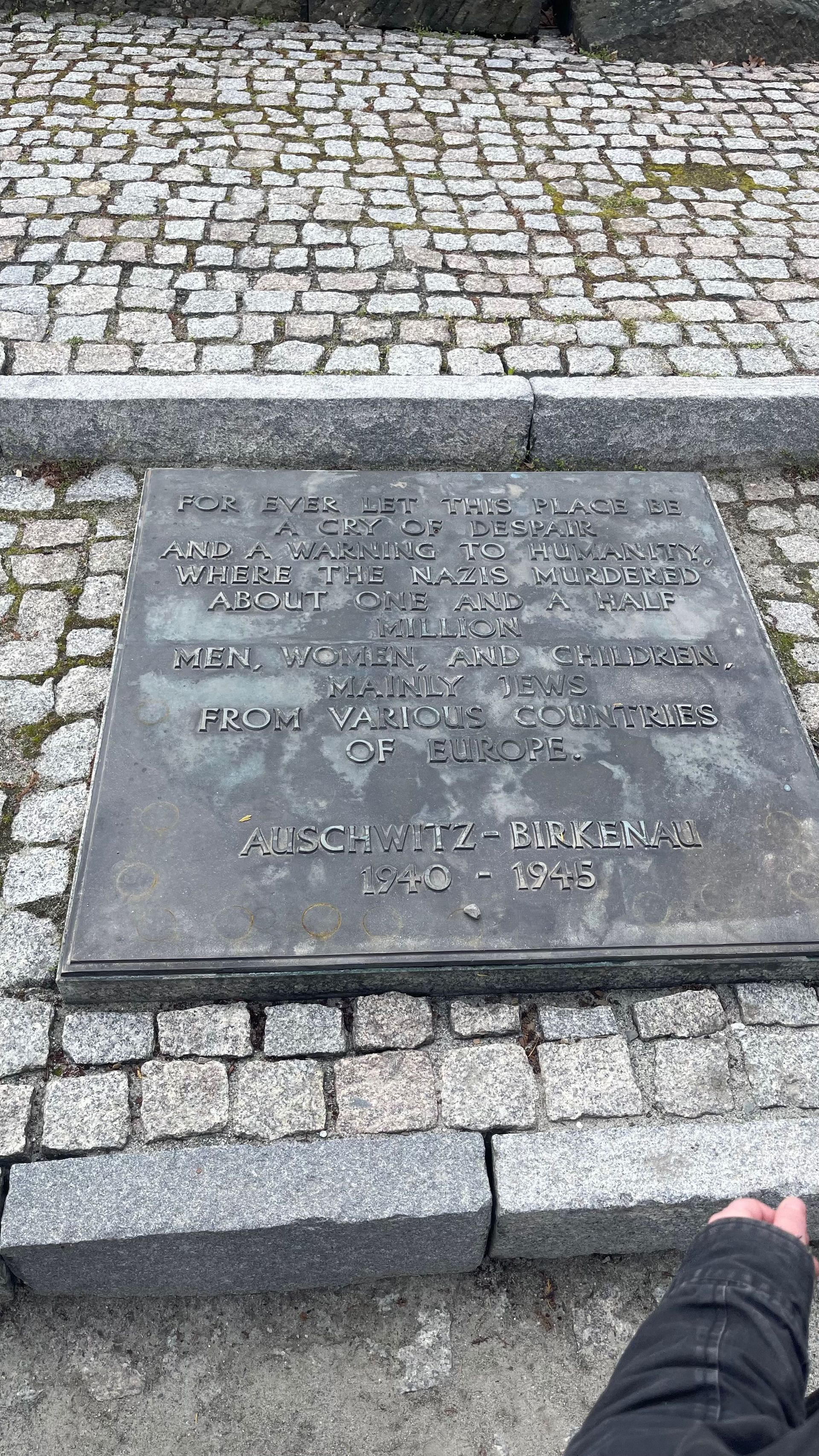 A rectangular metal plaque with engraved text, set in cobblestones, outdoors.