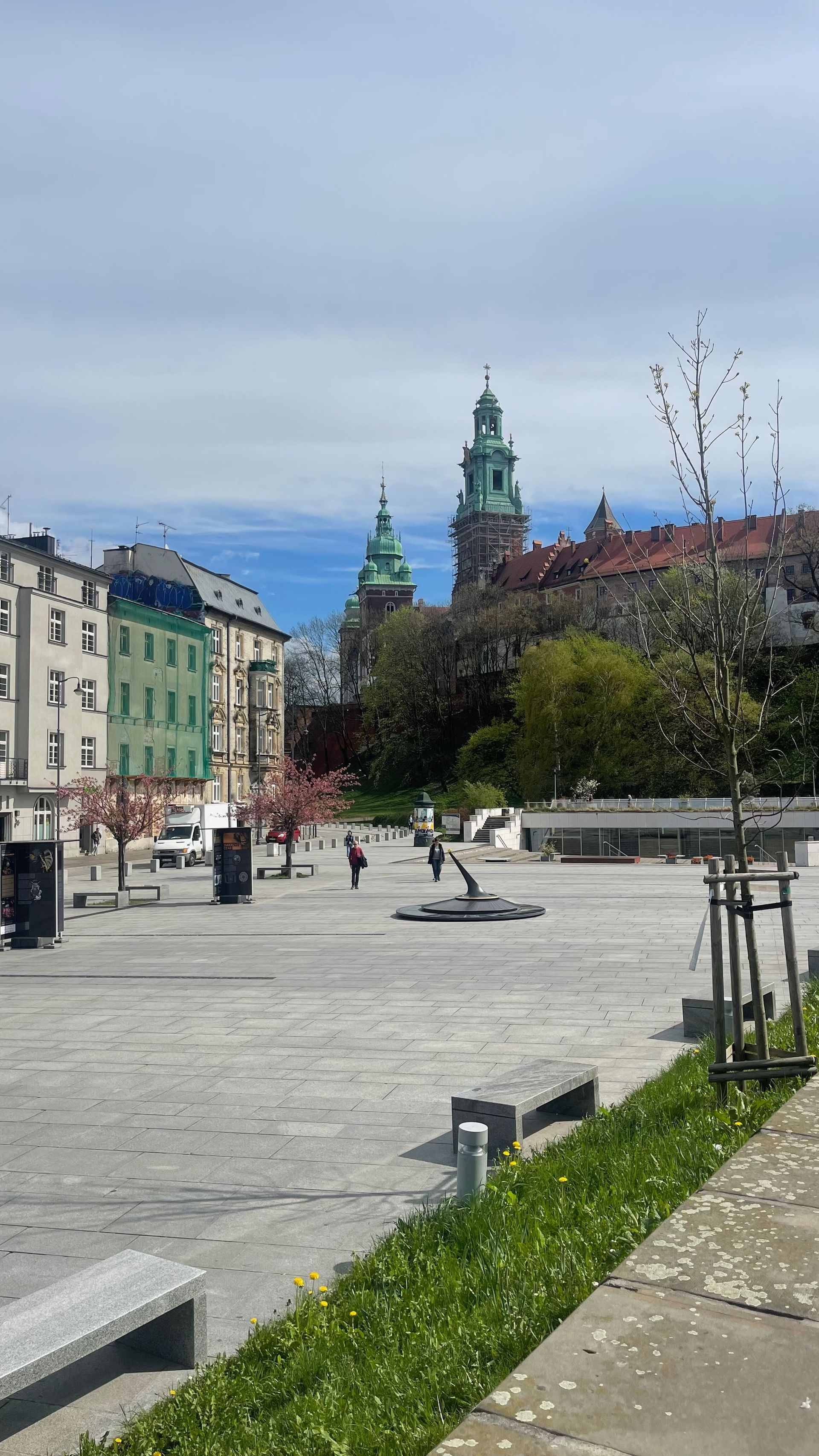 A square with a castle in the background, a few people, and colorful buildings.