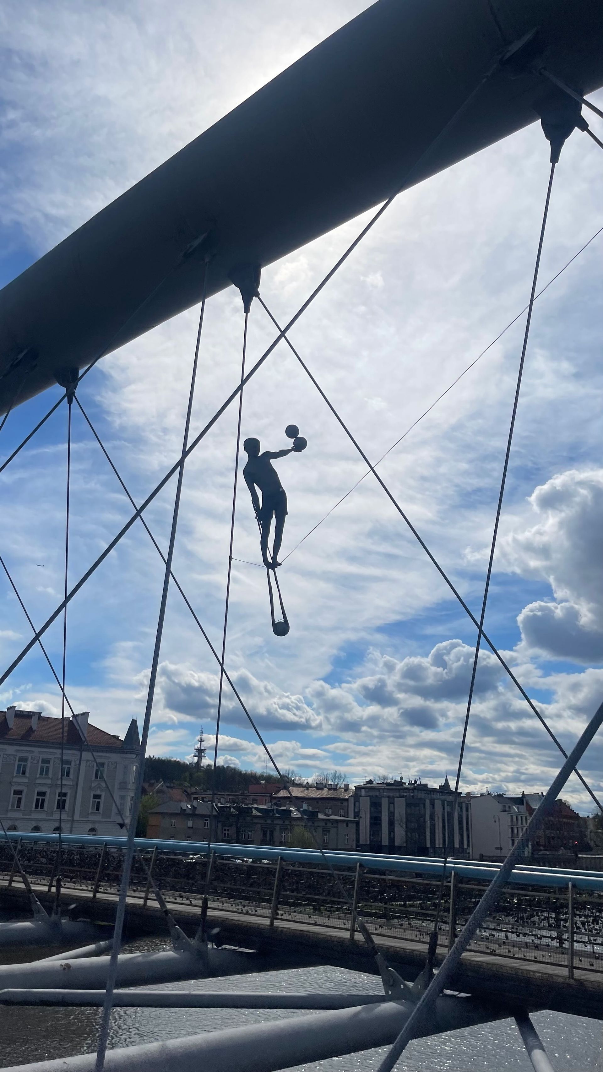 Silhouette of a tightrope walker on a bridge against a cloudy sky.