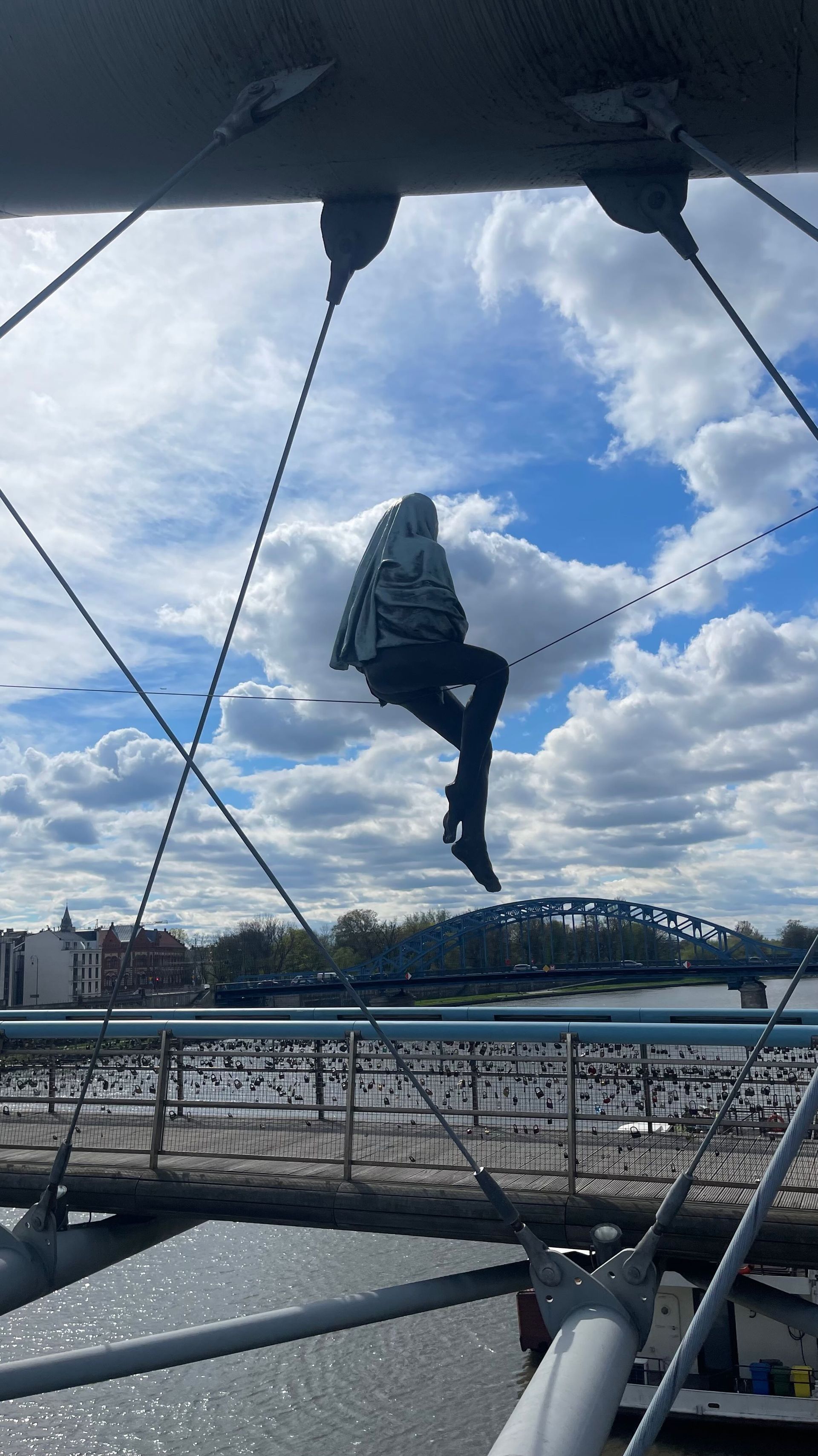 Person sitting on suspension bridge cables, overlooking river. Sunny day with clouds.