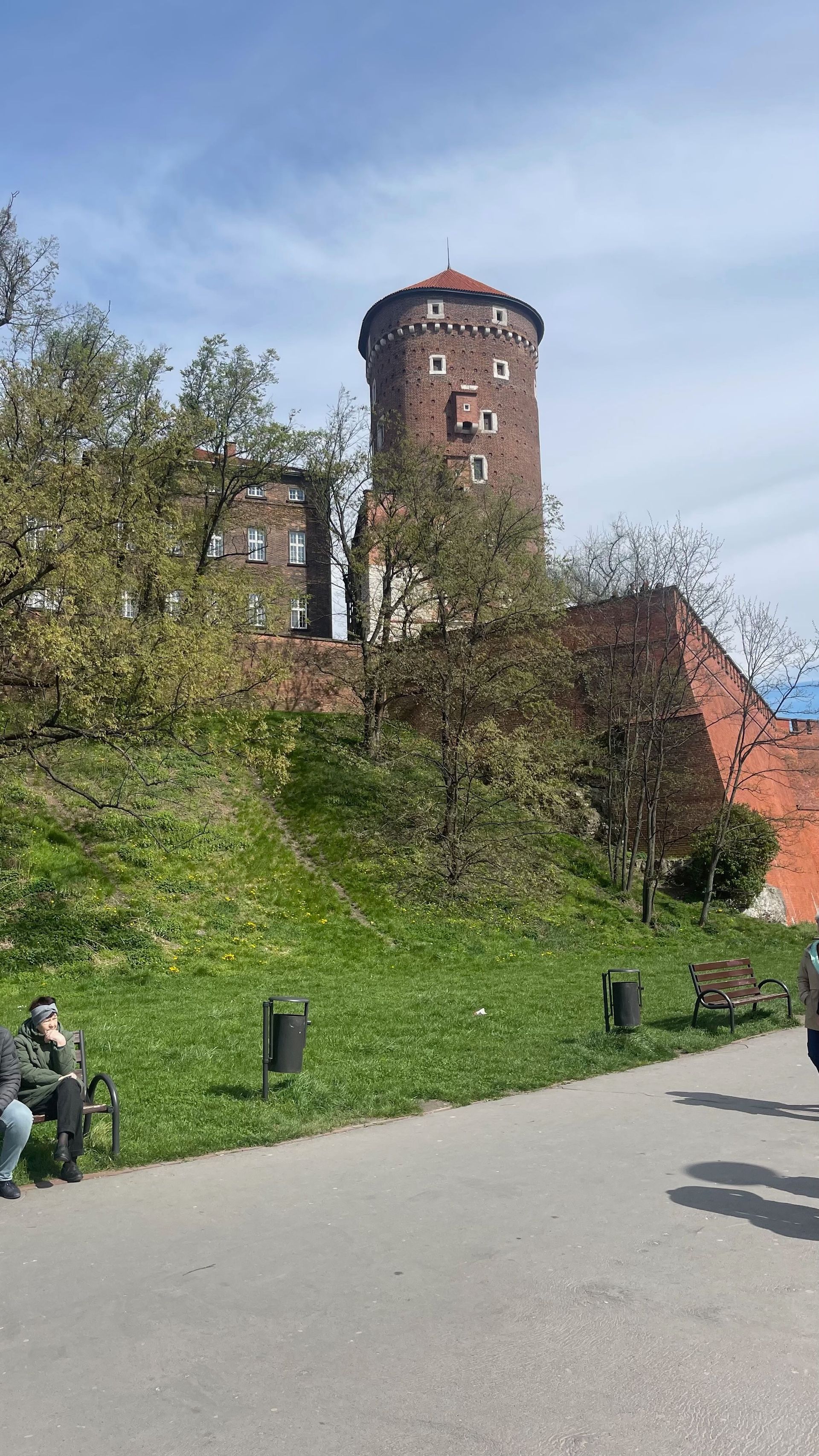 Stone tower atop a grassy hill with red brick walls, part of a historic building in Kraków, Poland.