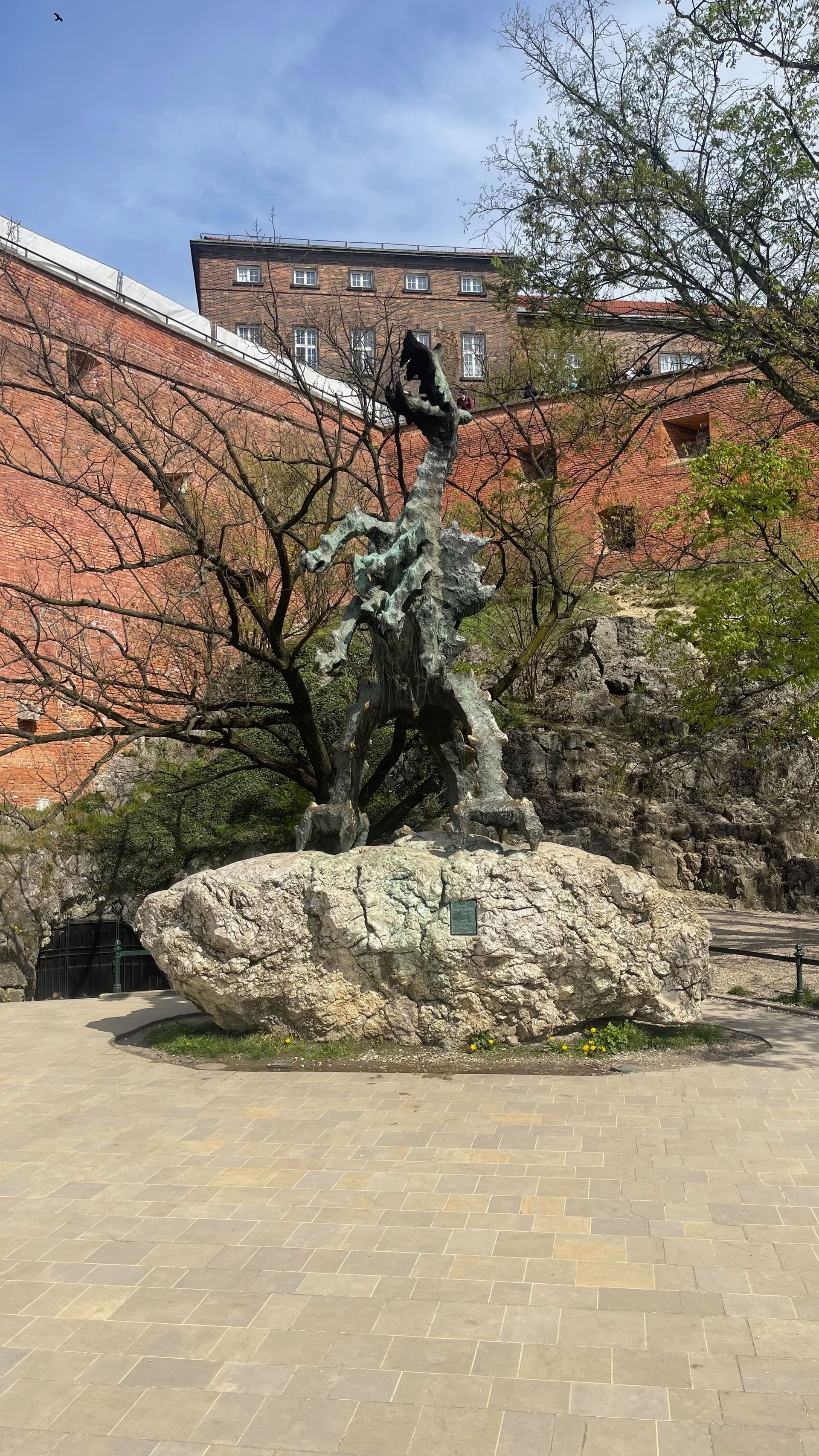 Bronze statue of a man on horseback atop a rock, set against a red brick building and trees under a blue sky.