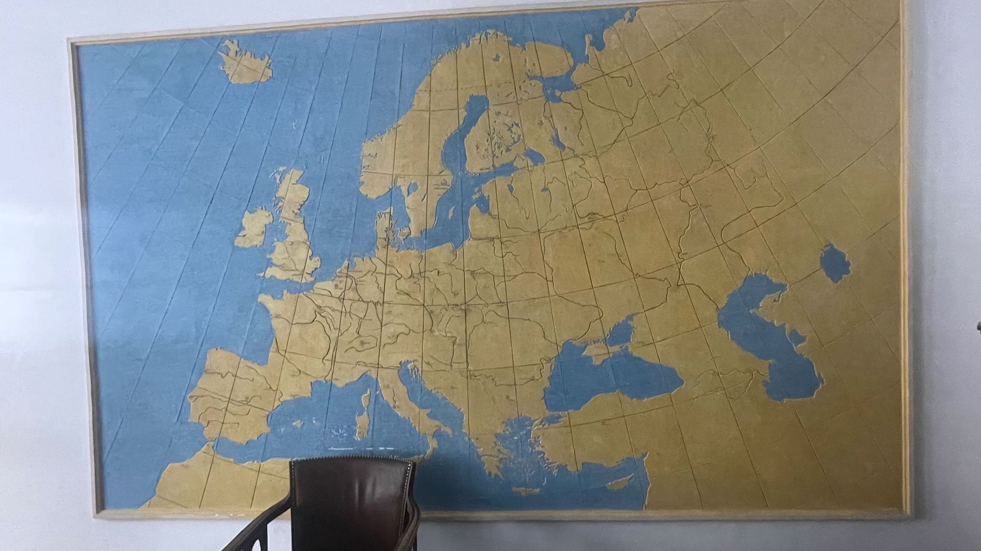 Map of Europe, golden landmasses against a blue background, mounted on a wall.