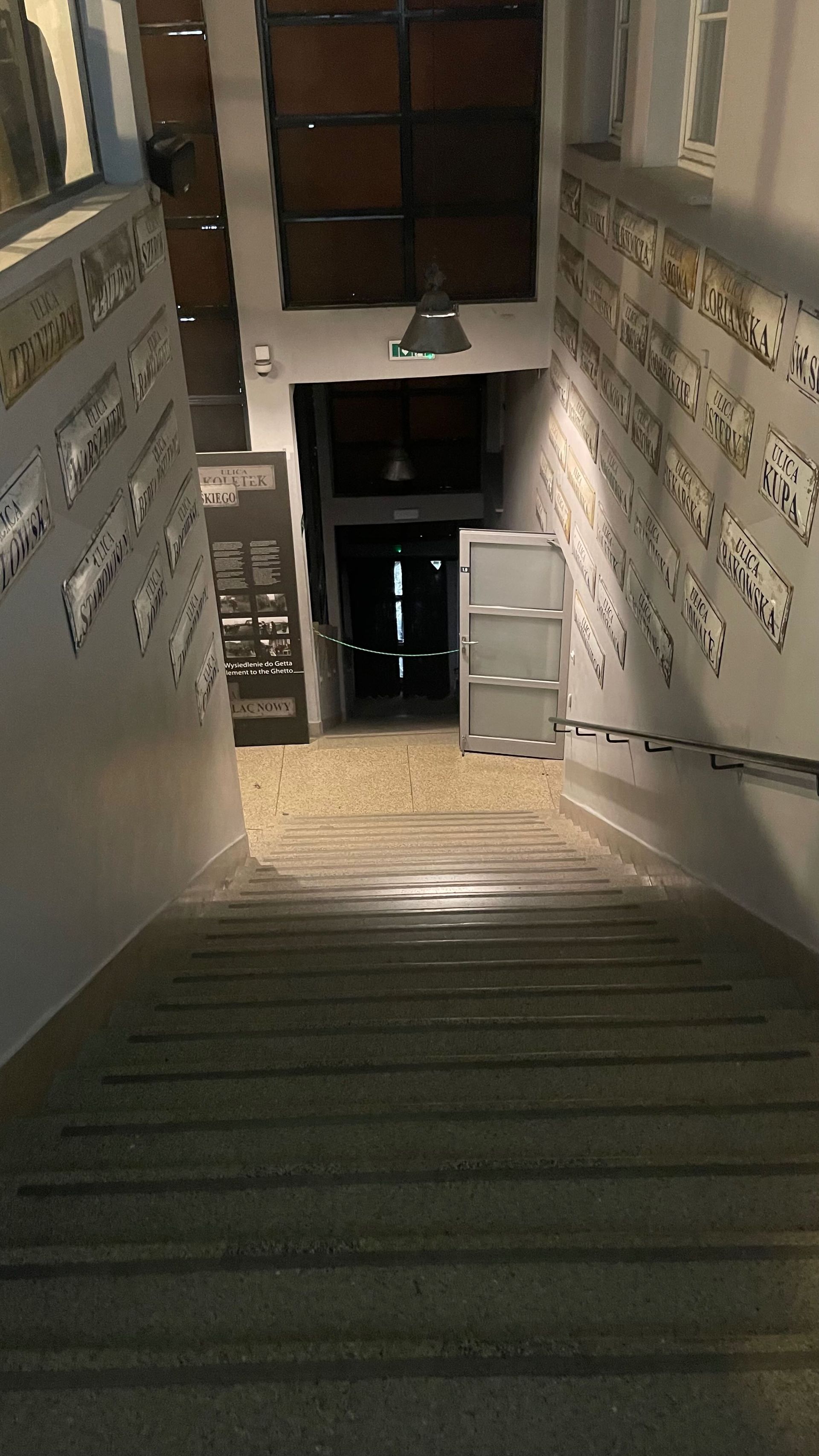 Staircase leading downwards; walls decorated with informational displays, dark doorway at the end.