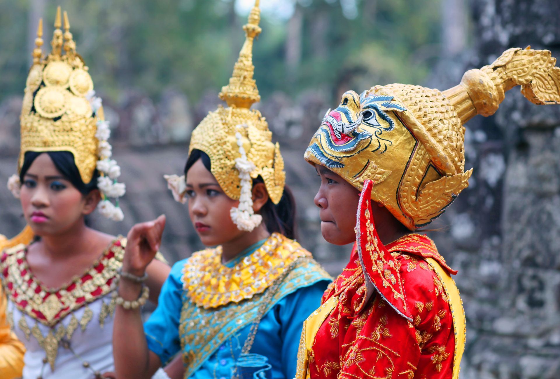 Three Cambodian dancers in ornate golden headdresses and colorful costumes; outdoors.