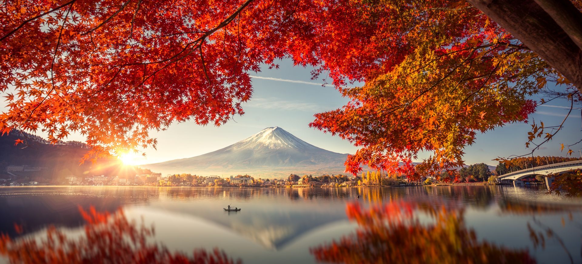 Red autumn leaves frame a lake with Mount Fuji in the distance.