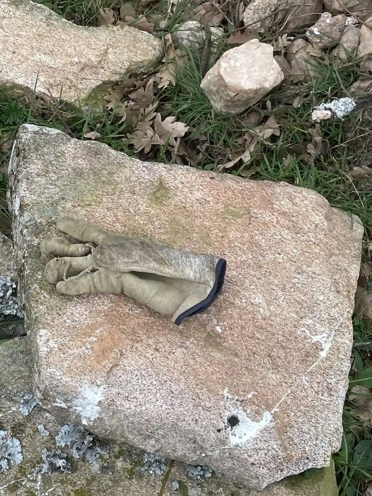 Guante de trabajo con correa negra sobre una gran roca al aire libre entre piedras más pequeñas.