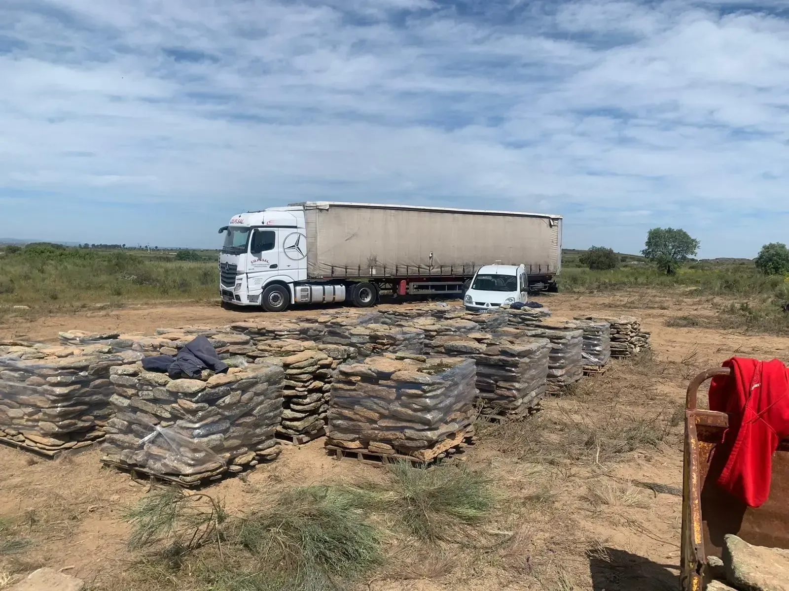 Camión y furgoneta blanca cerca de sacos apilados en un campo rural seco.