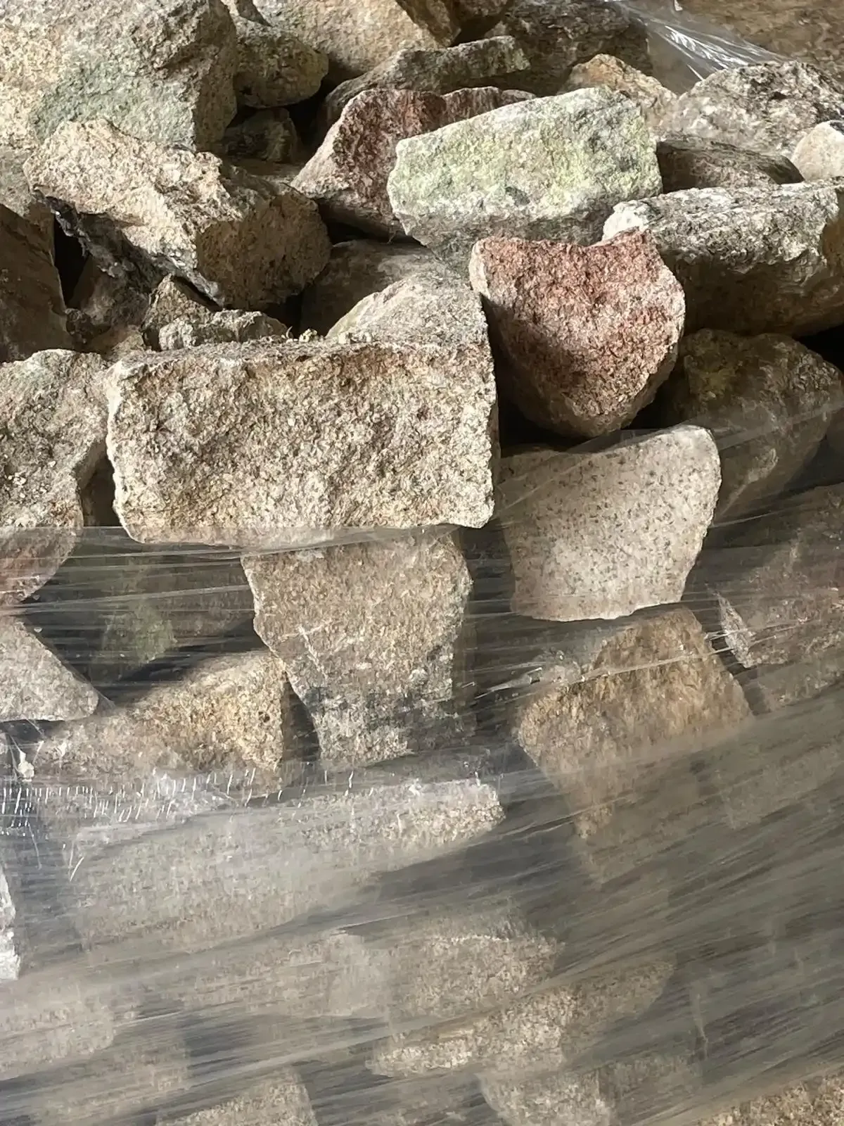 Piedras toscas apiladas de color beige y tostado con algunas rocas más oscuras en una vista de cerca.