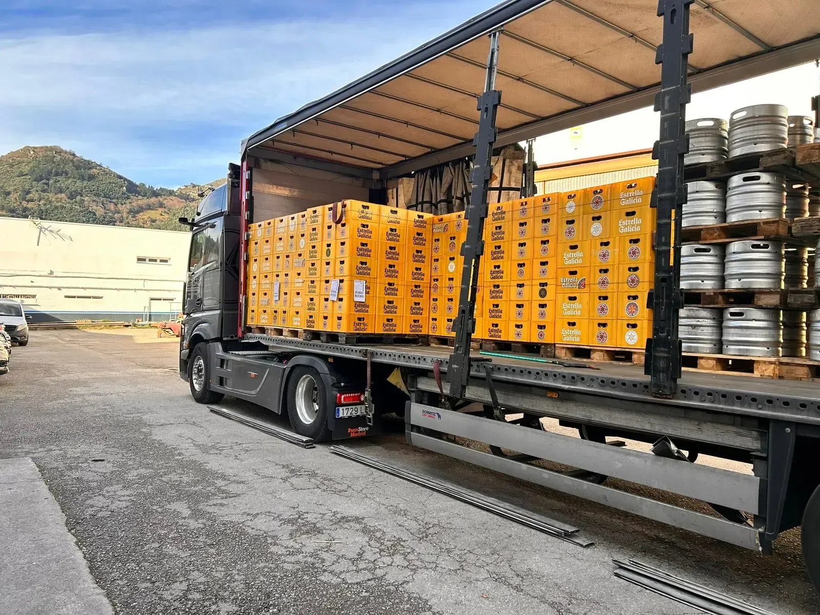 Camión cargado con cajas de naranjas apiladas en una plataforma en un patio industrial al aire libre.