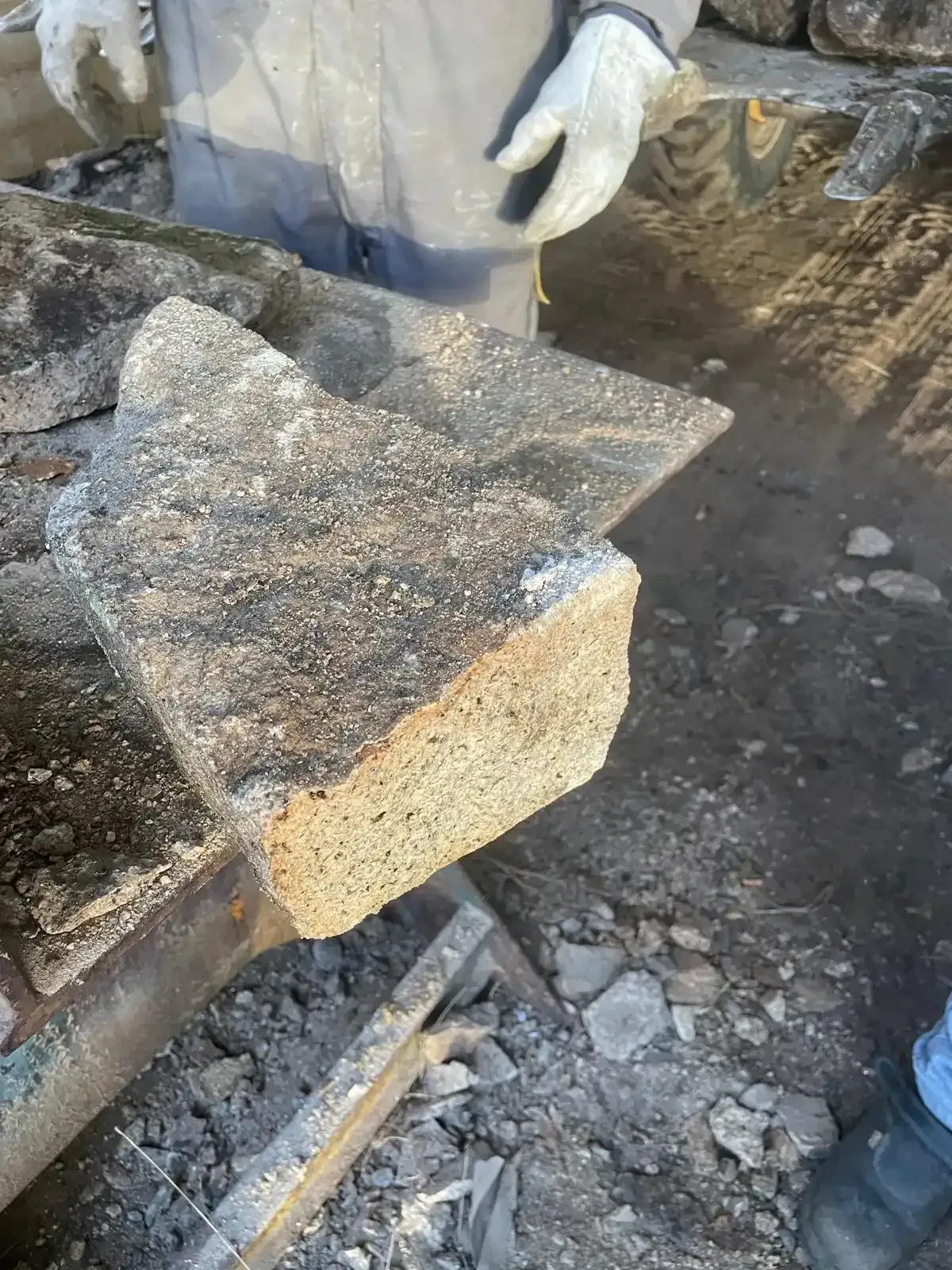 Un trabajador sostiene un bloque de piedra tosca sobre una obra en construcción polvorienta.