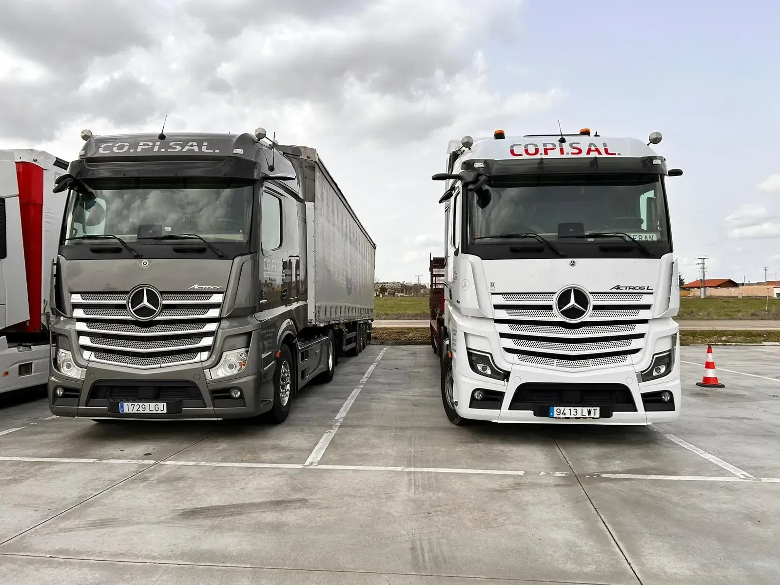 Dos camiones Mercedes blancos estacionados uno al lado del otro en un terreno mojado bajo un cielo nublado.