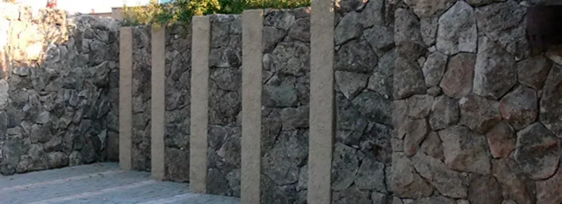 Postes de hormigón junto a un muro de contención de piedra a lo largo de un sendero pavimentado.
